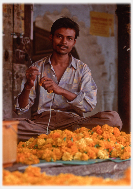 Man making garlands sitting behind pile of flowers