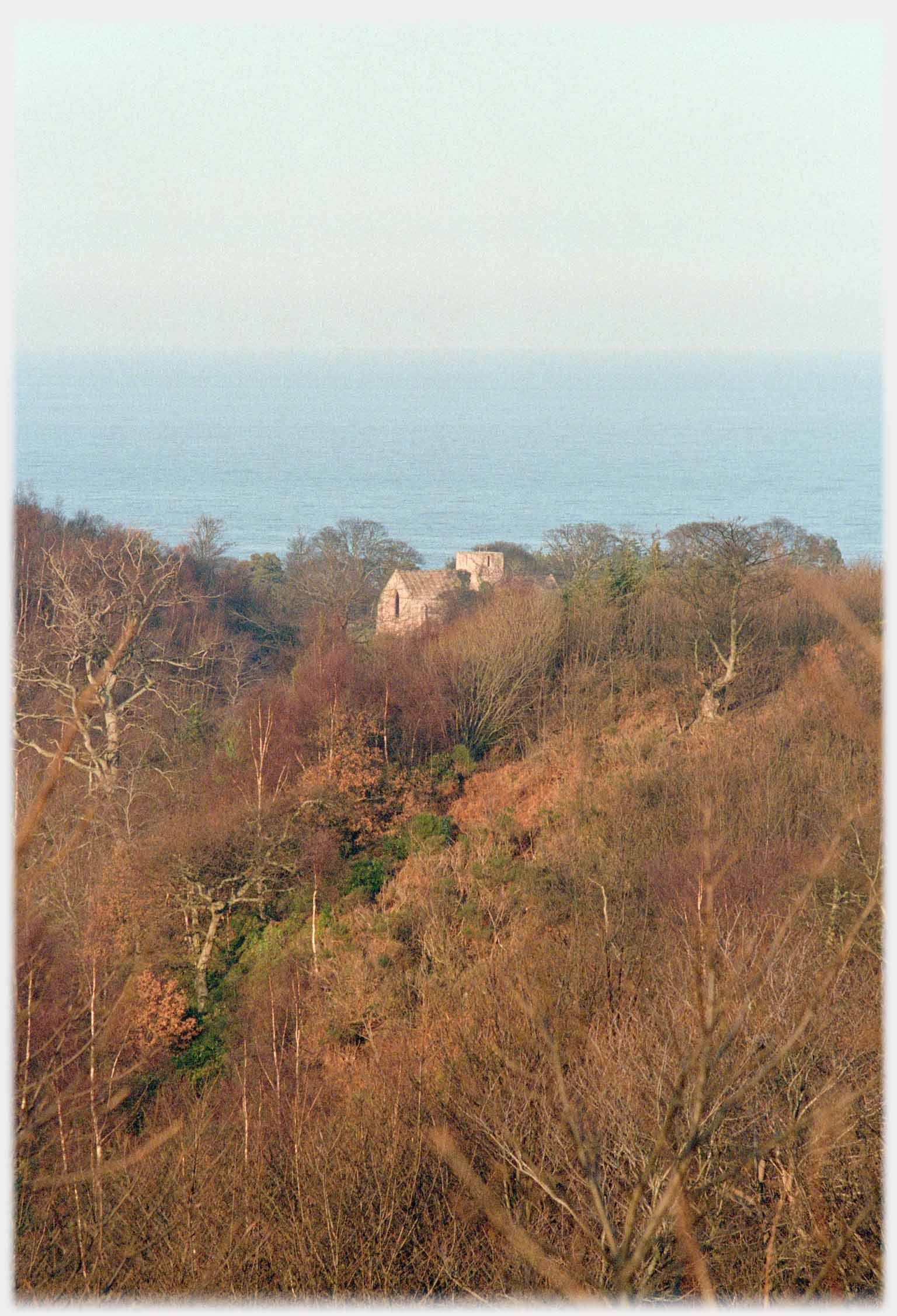 Towered building among trees, sea beyond.