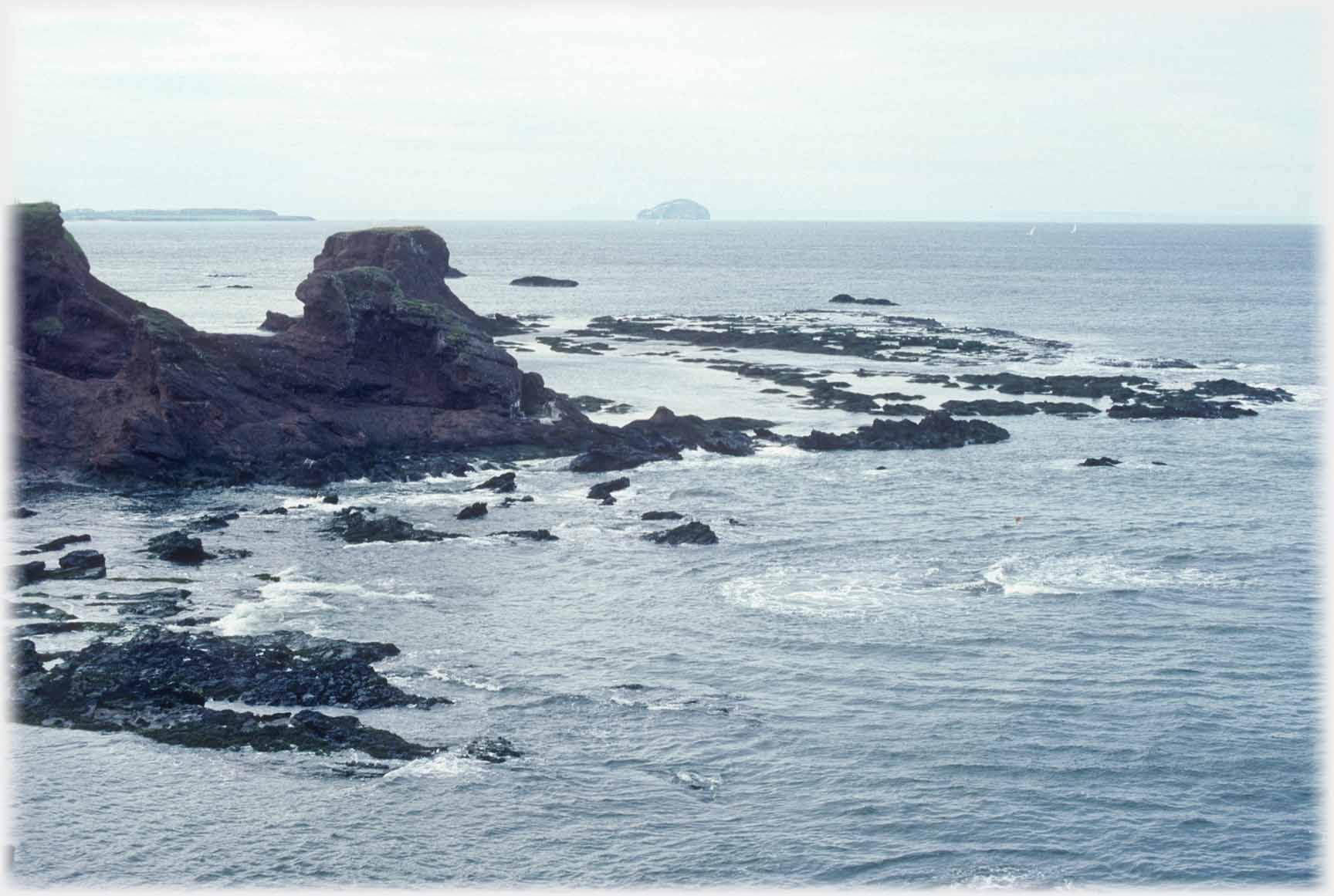 Sea rocks below shore rocks with Bass Rock on the distant horizon.