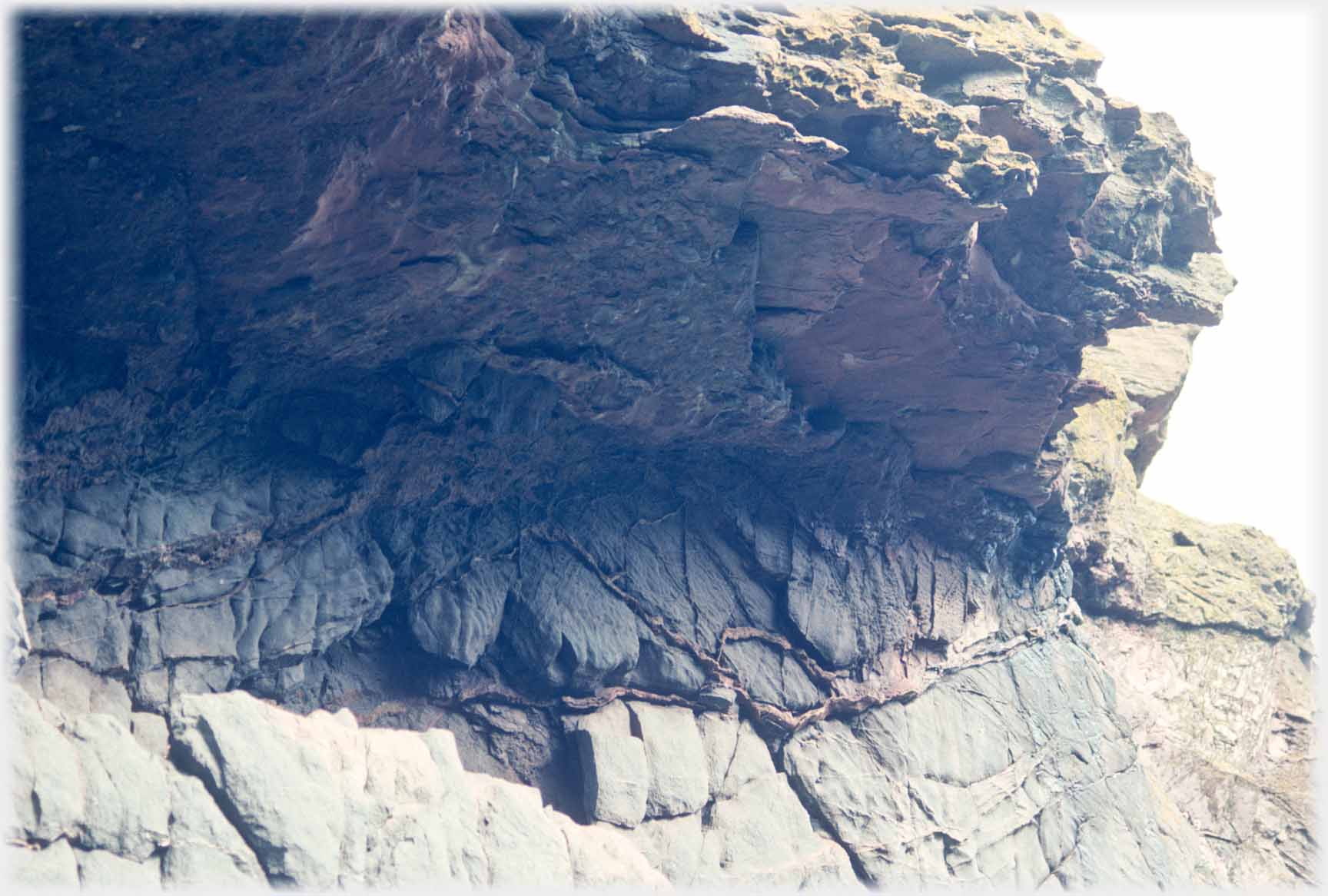 A rock surface where undulating lines of quite different rock appear from the cracks.