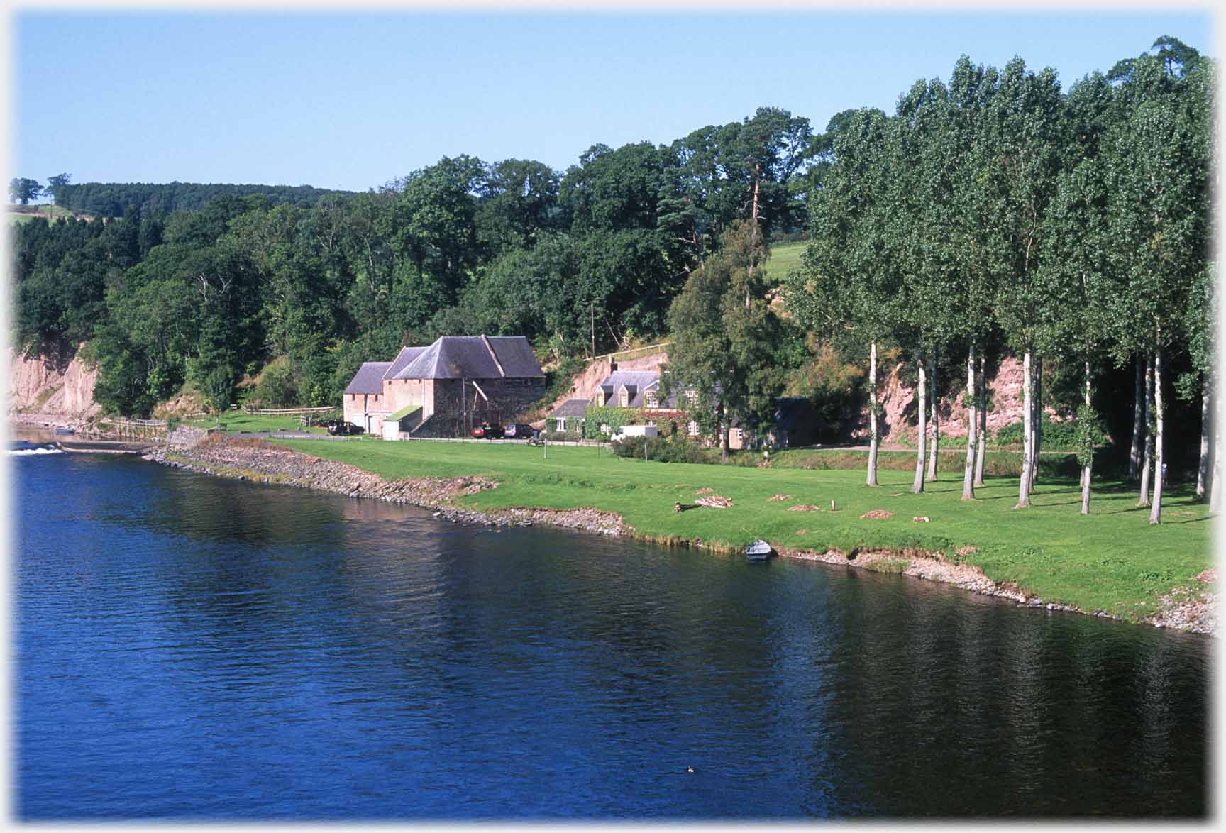 Buildings on riverbank, trees to right.