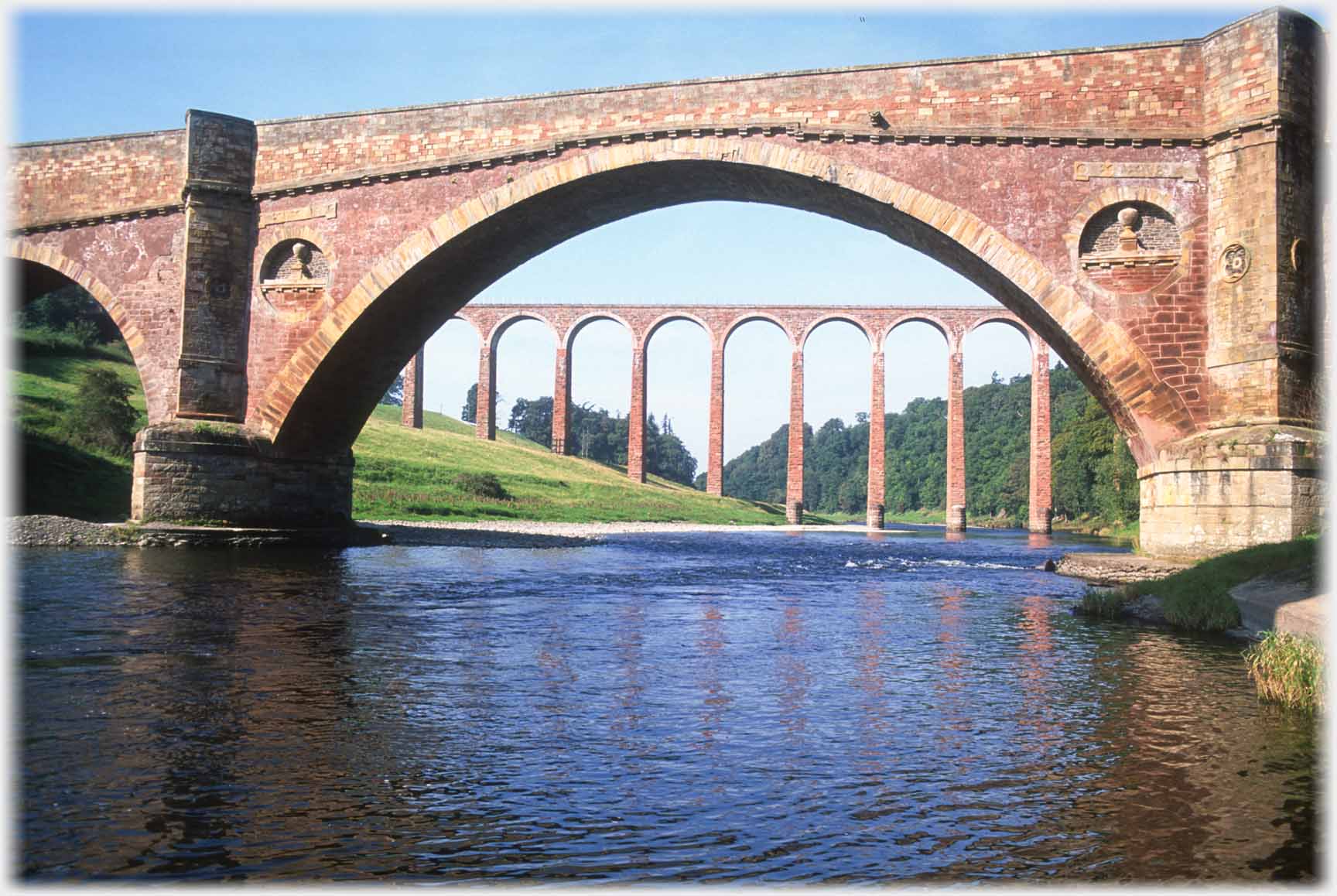 Viaduct seen through arch of bridge which has decorations in stonework.