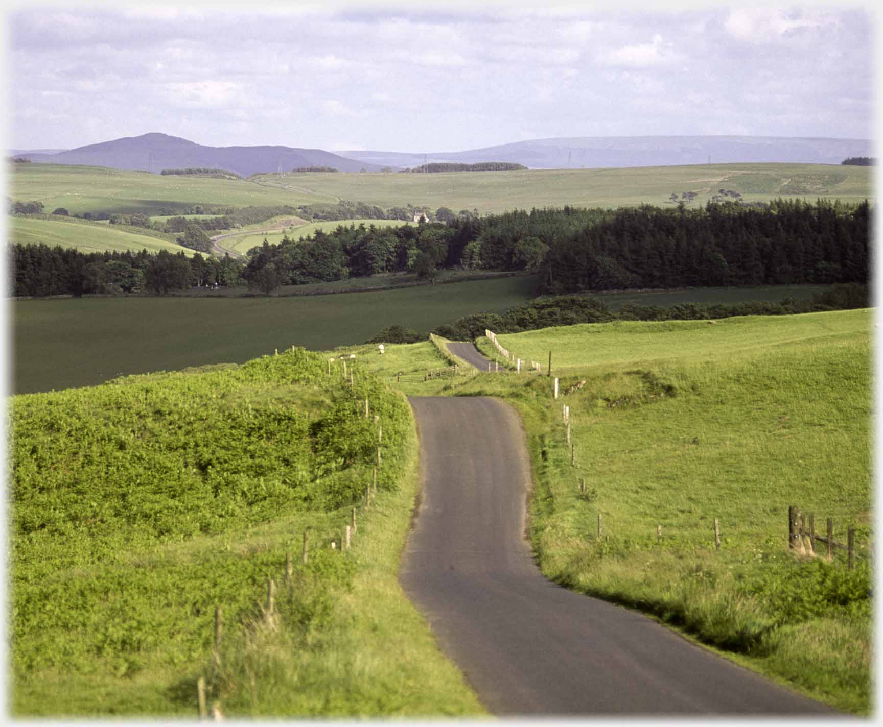 Road descending down hil-folds reappearing and pointing at volcano shaped hill.