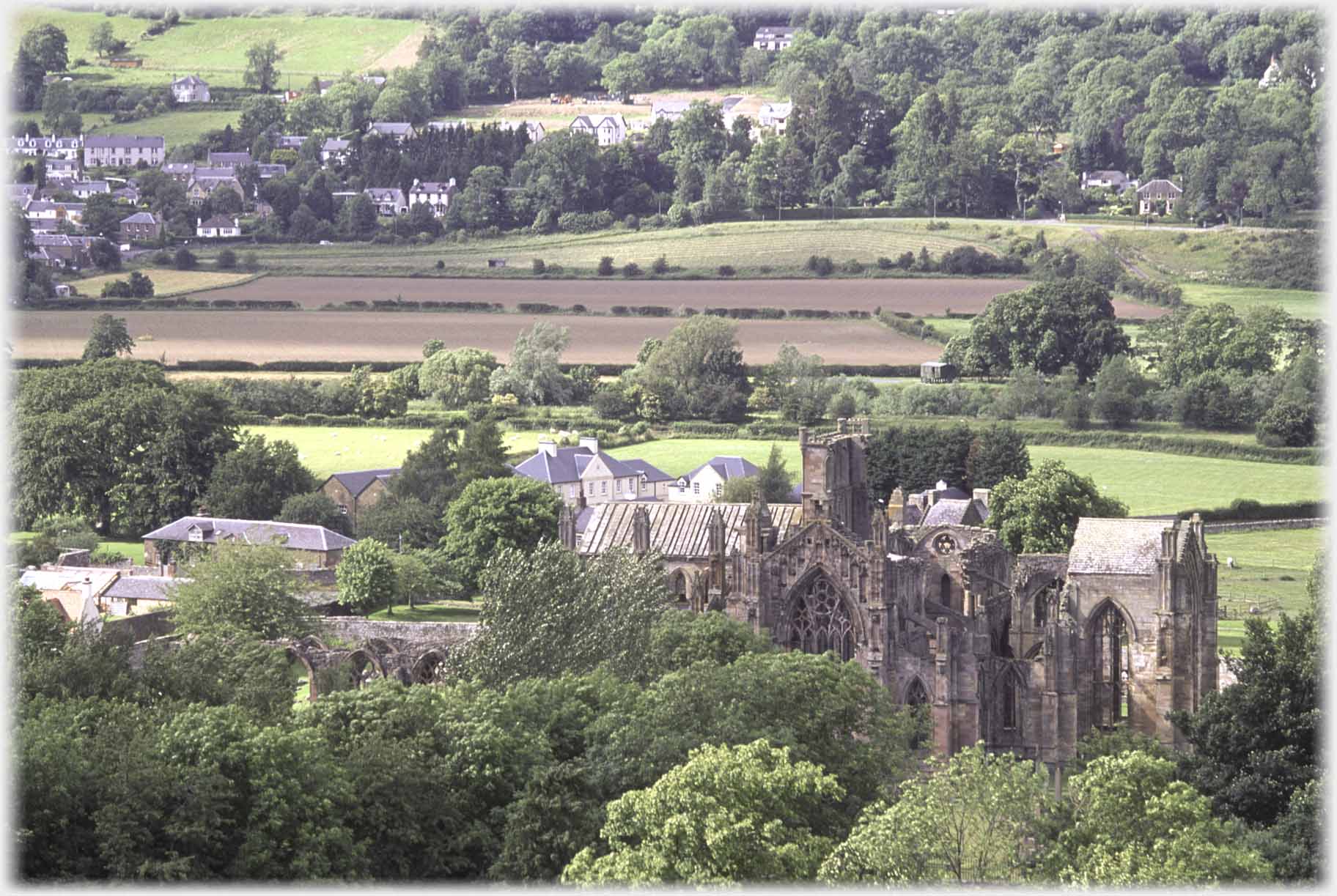 Abbey amongst trees with fields beyond.