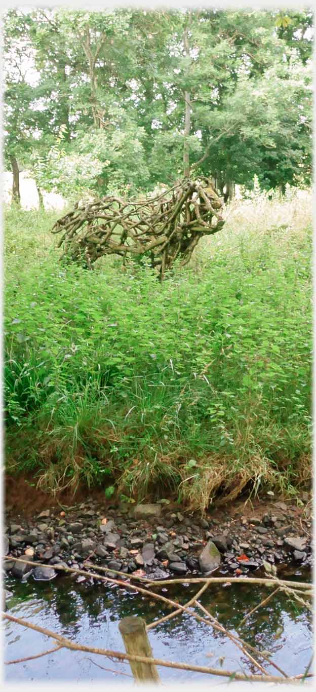 Stream with bull made of roots in field beyond.