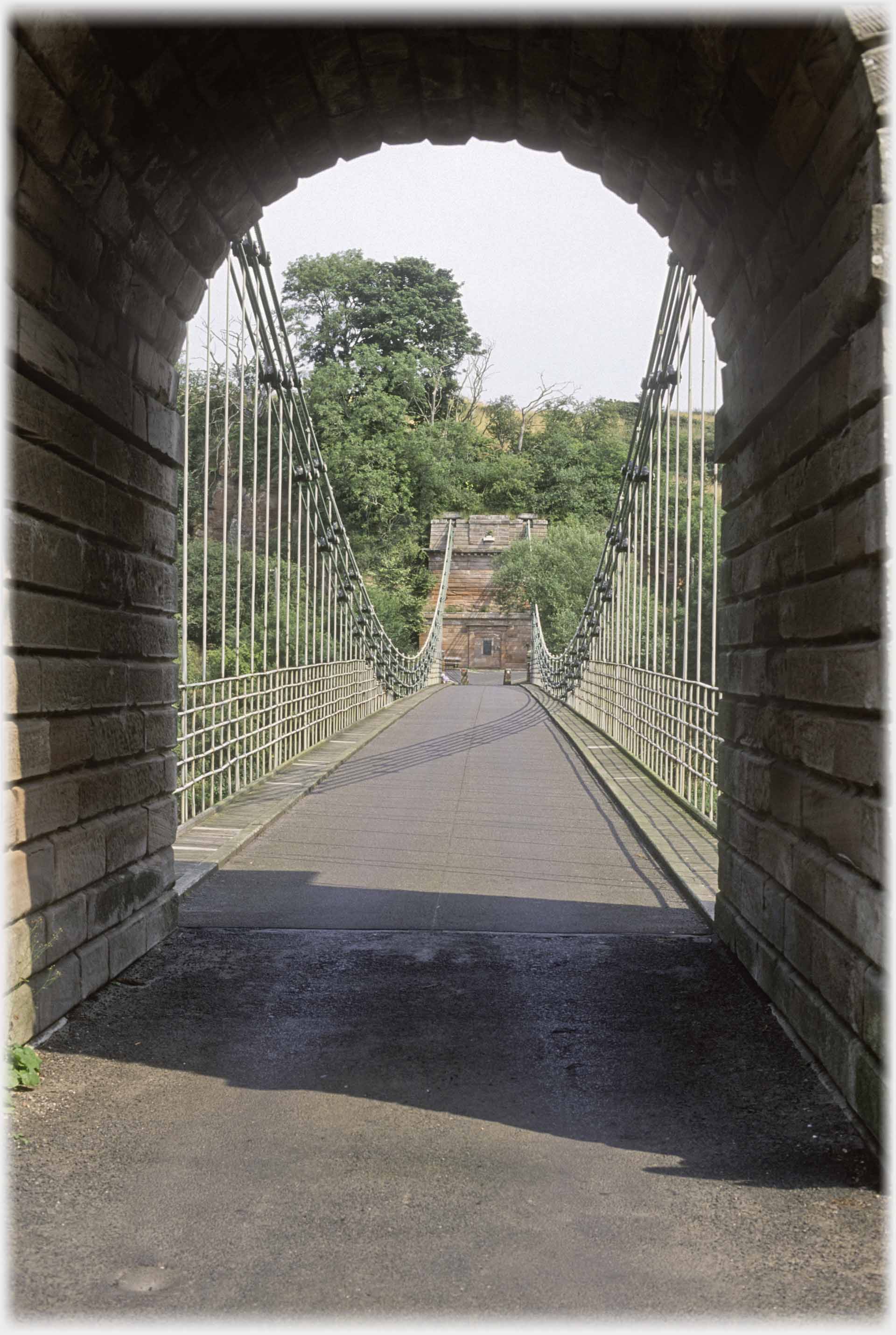 Looking from inside arch of one pillar along a suspension bridge.