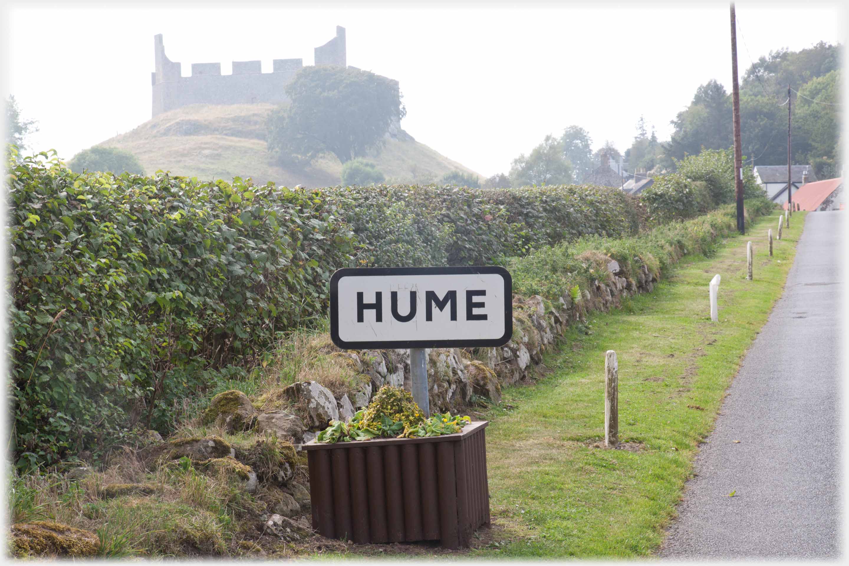 Village name sign with ruined castle on hill beyond.