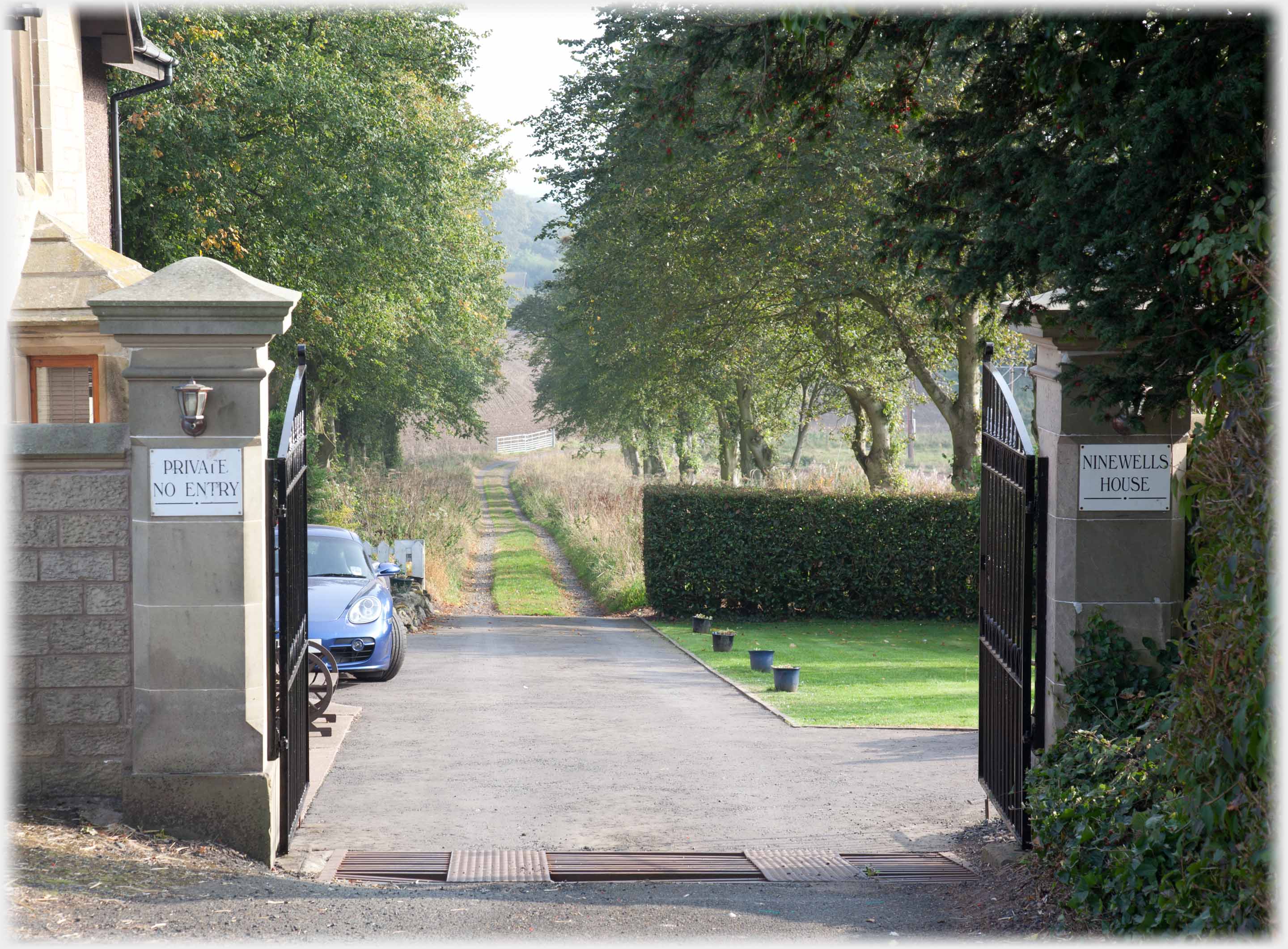 Gates and lodge house with drive leading away between trees. Ninewells House on gate pillar.