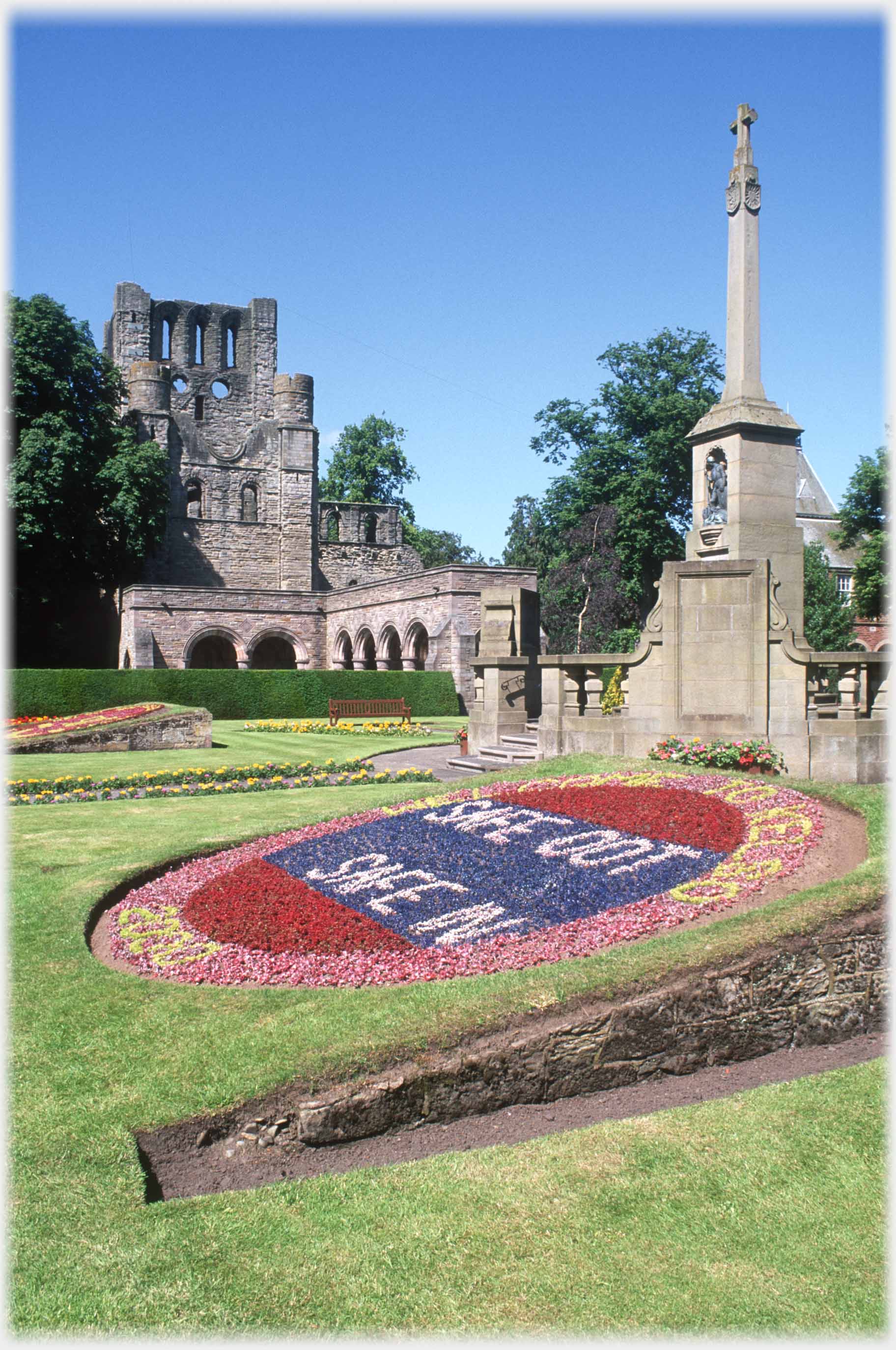 Ruined abbey with monument and floral dispaly in foreground.