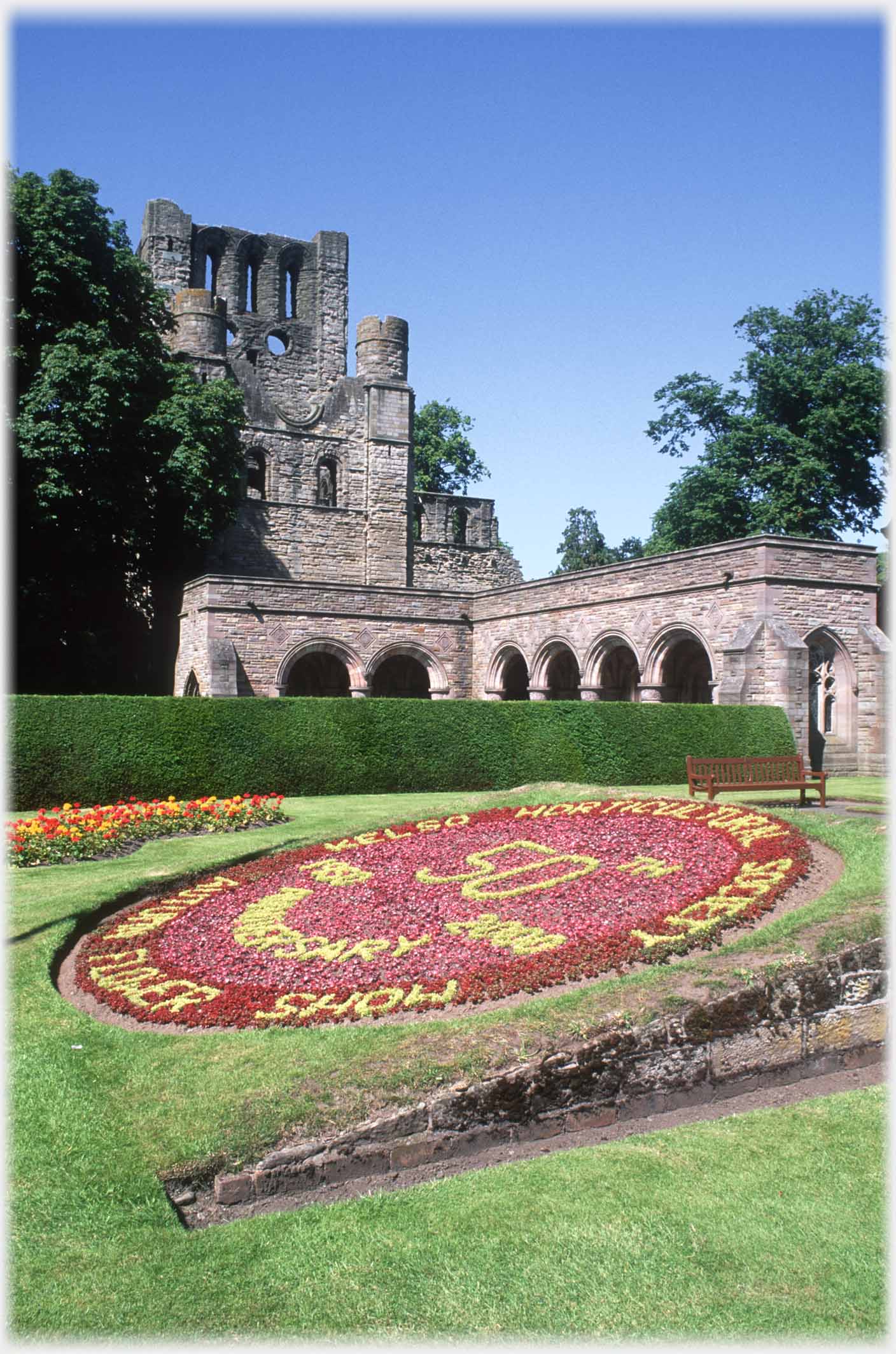 Ruined abbey with floral display in foreground.