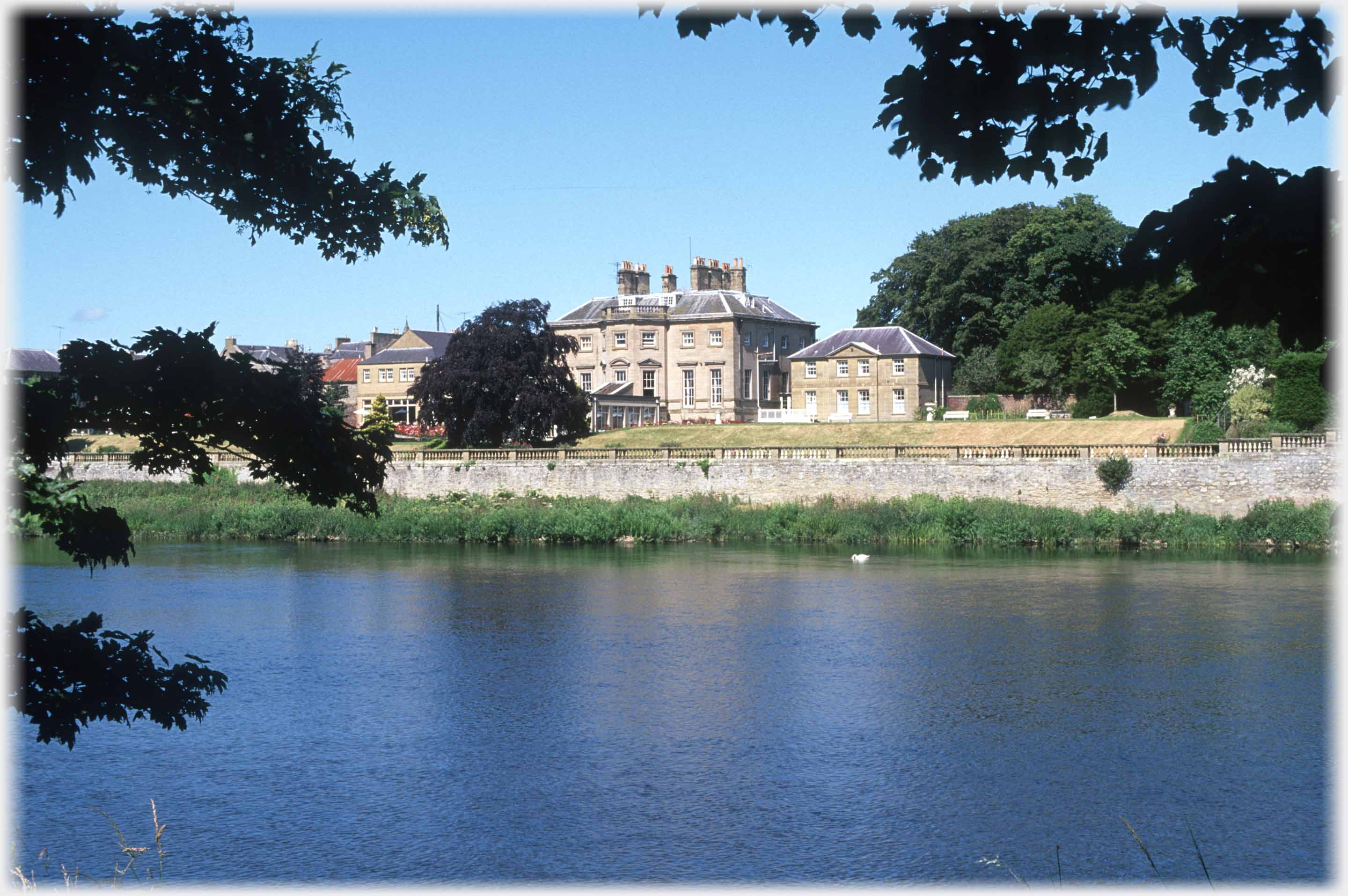 Large house seen across river between trees.