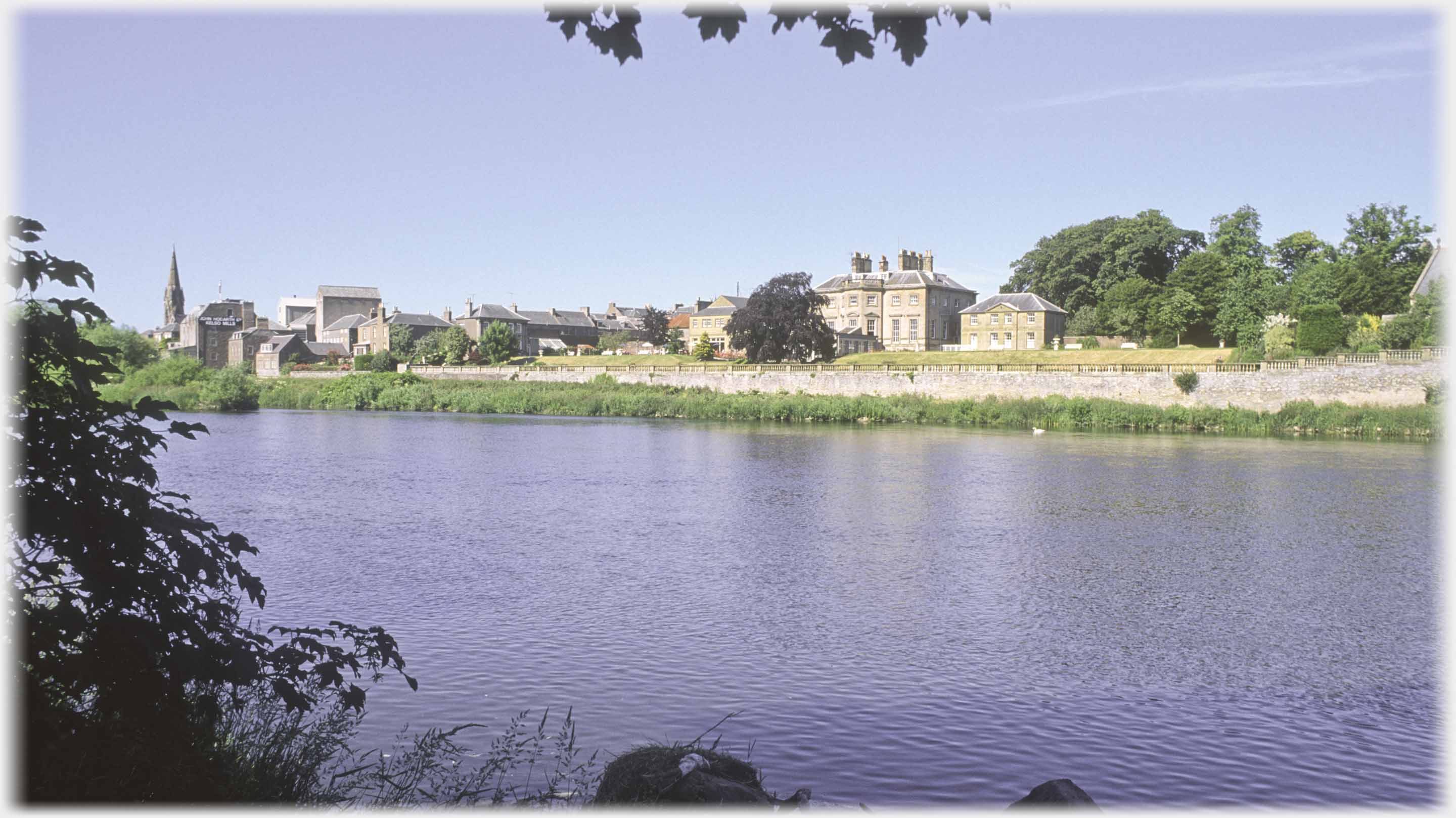 Large house across river, spired church to left.