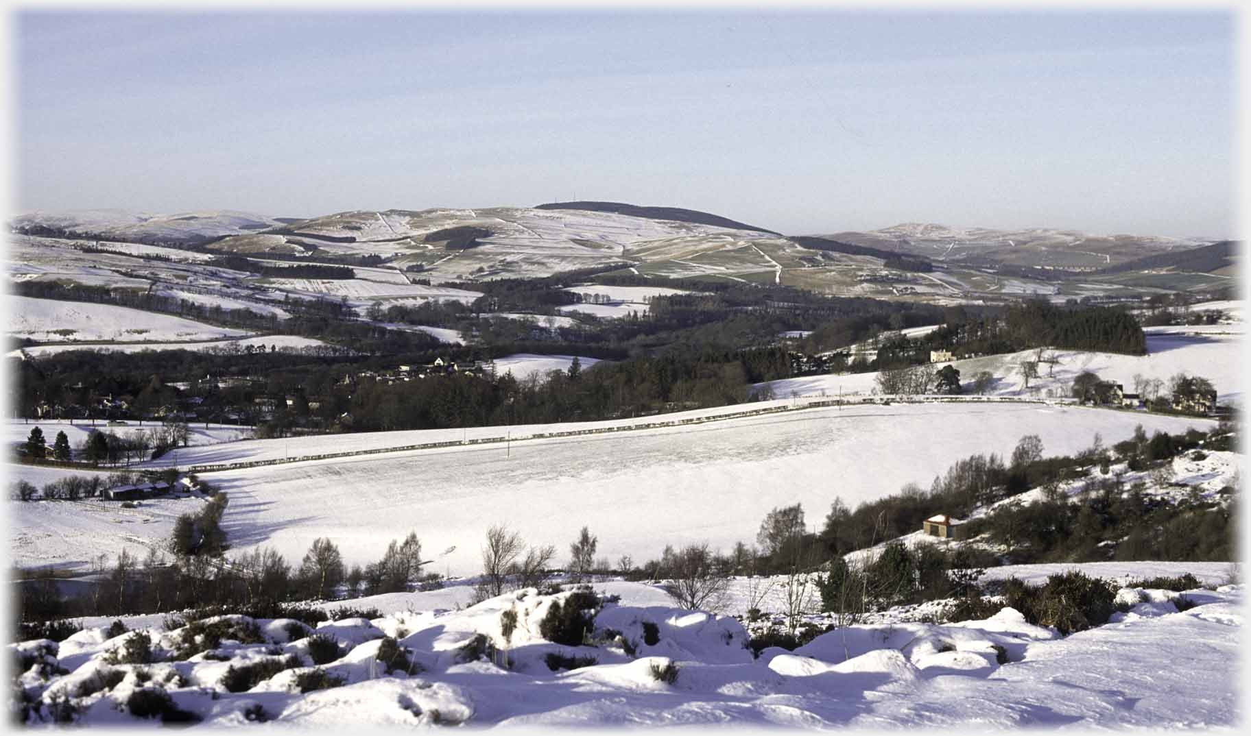 Winter with light snow across treed valley and nearby hills.