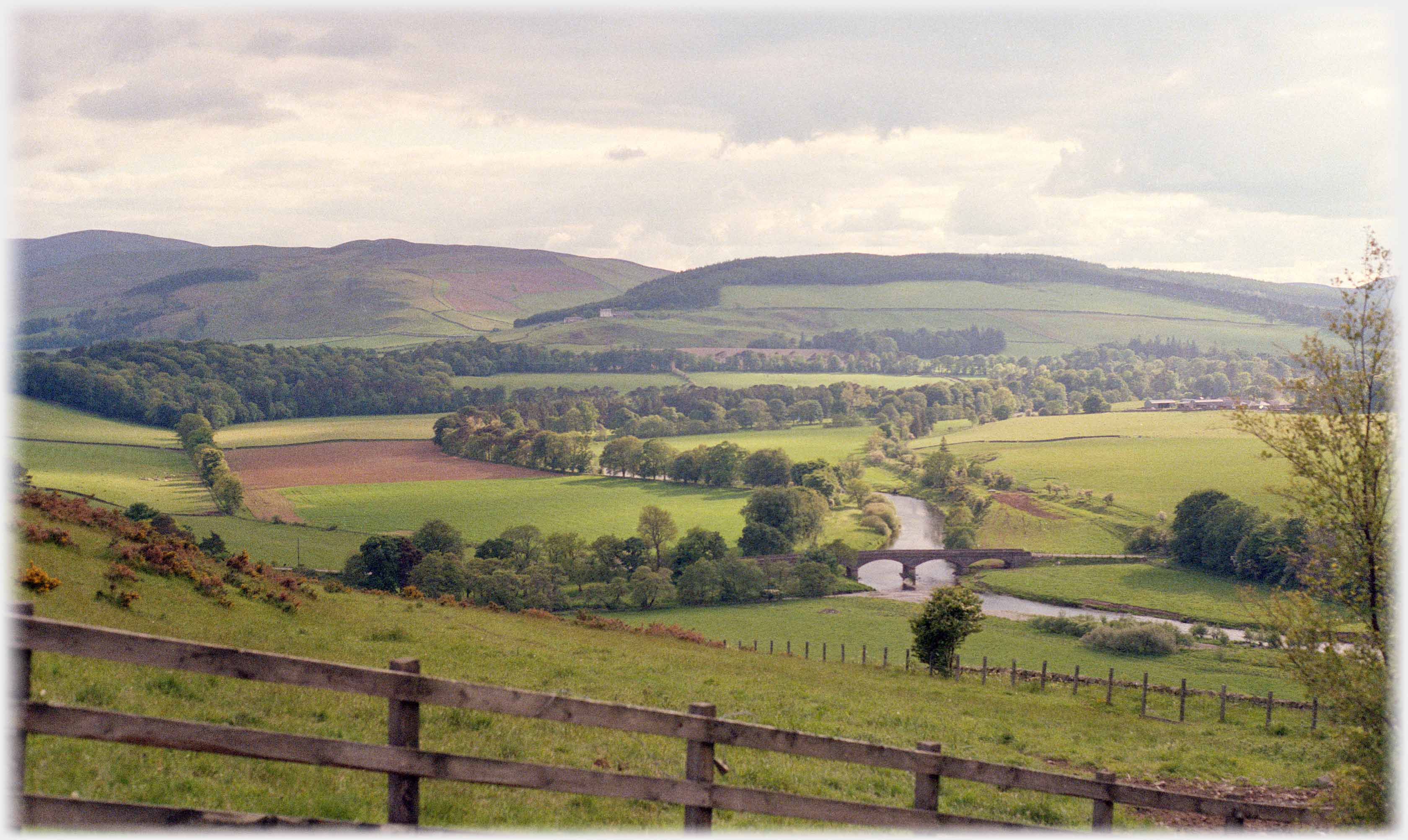 Looking down over valley of fields and trees with river running under bridge.