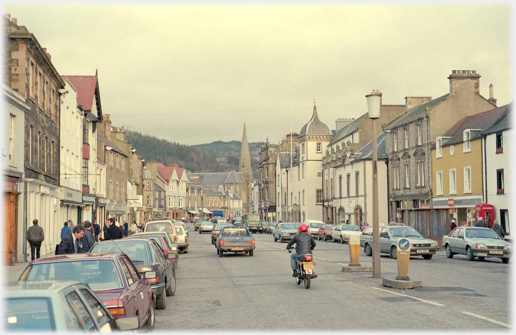 Wide shopping street with parked cars and traffic.