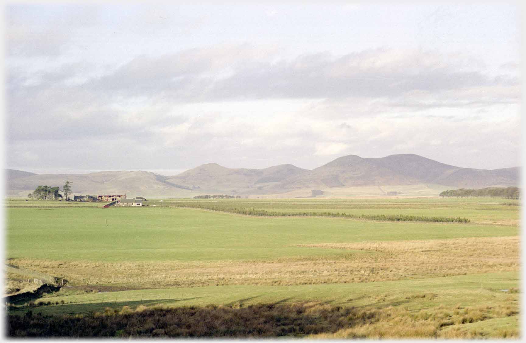 Farm on open flat country with backdrop of a line of hills.