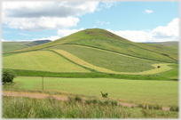 Hill with tractor ploughing a curved path at its foot.