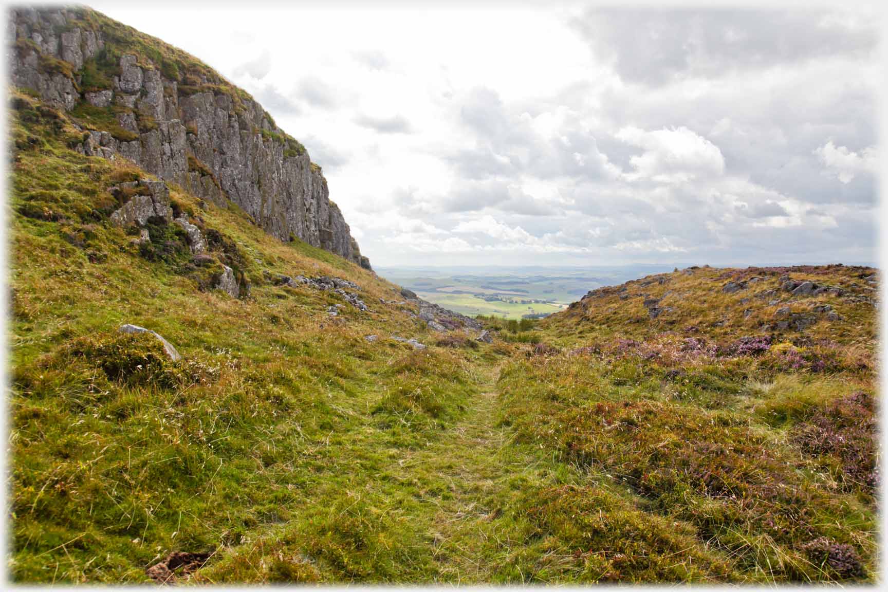 Cliff formation with grass and heather area below.