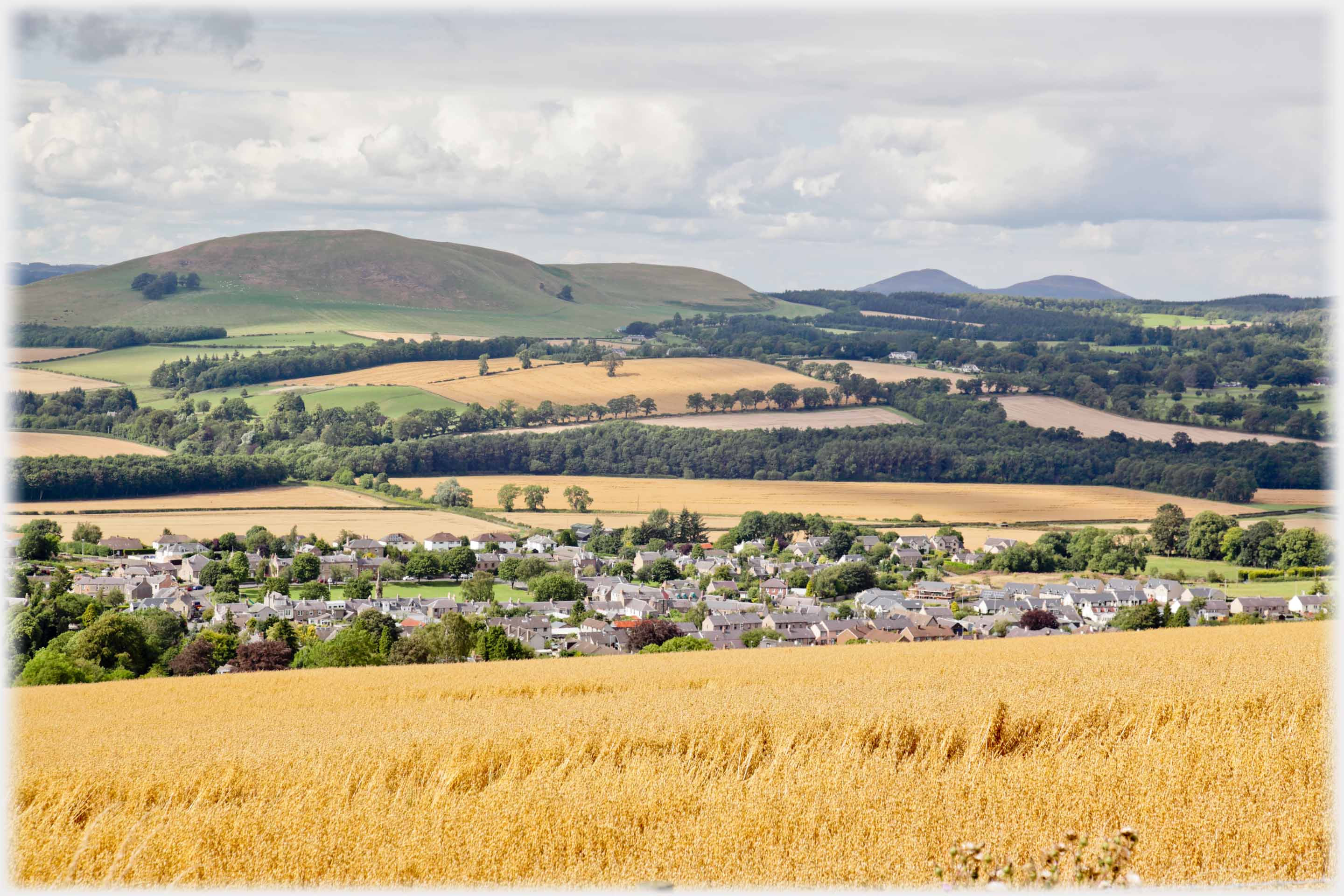 Village with corn fields, hill beyond, and to right distant pair of hills.