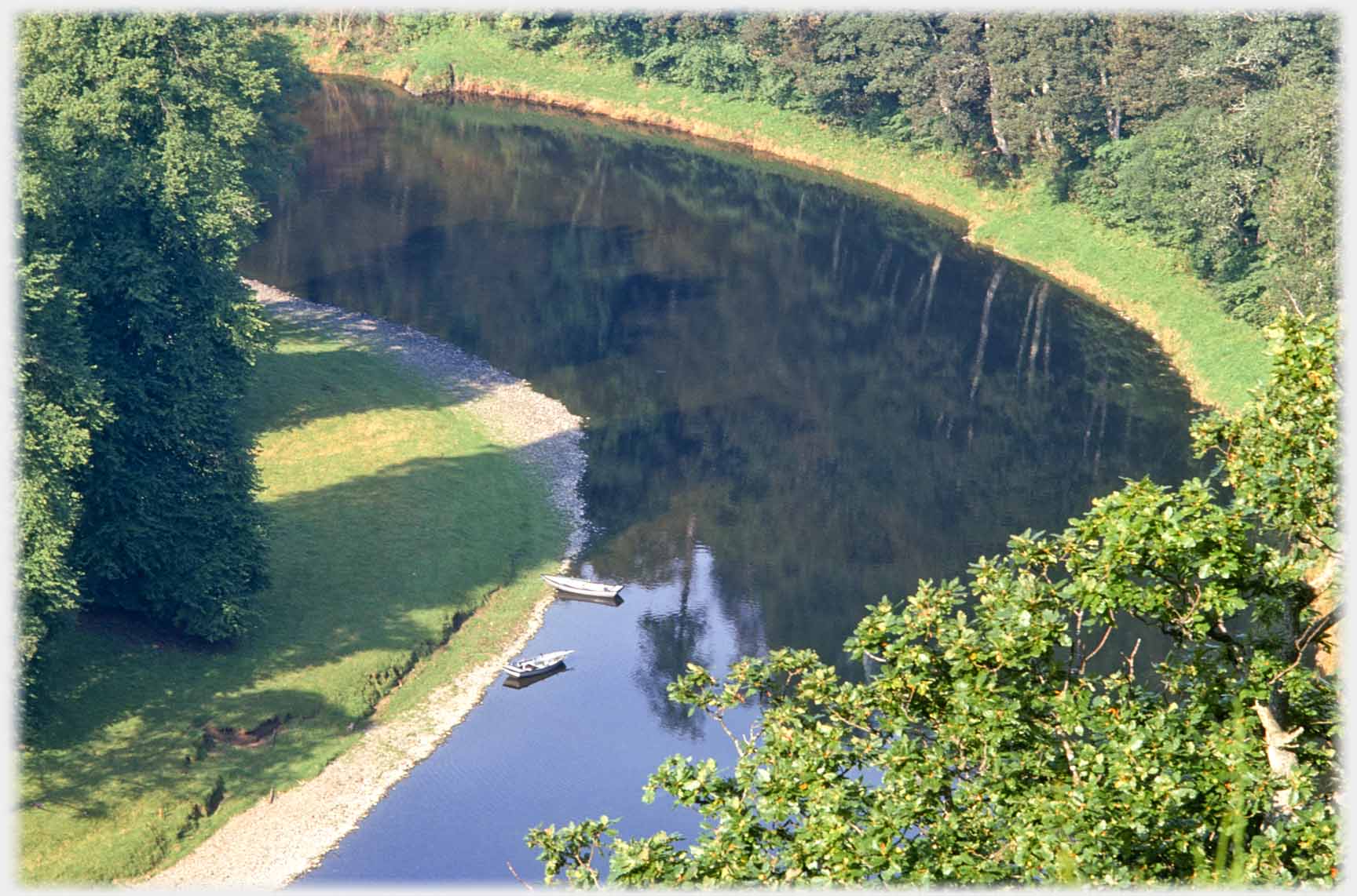 Curved river with two boats and reflections of trees.