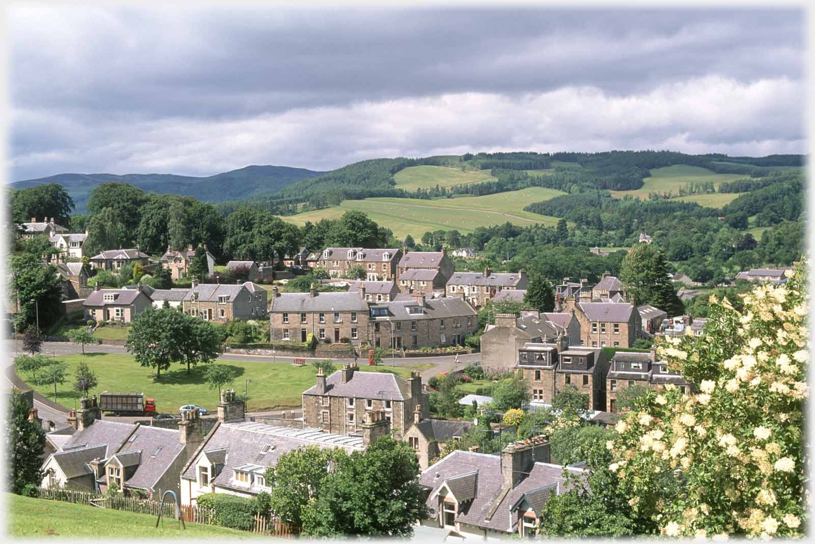 Irregularly laid out houses with well treed hillside above them.