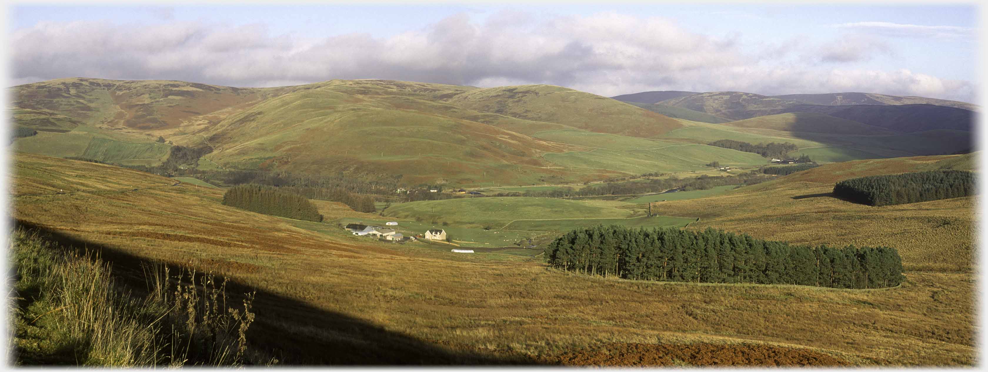 Panaramic view of wide valley with farm building in centre.