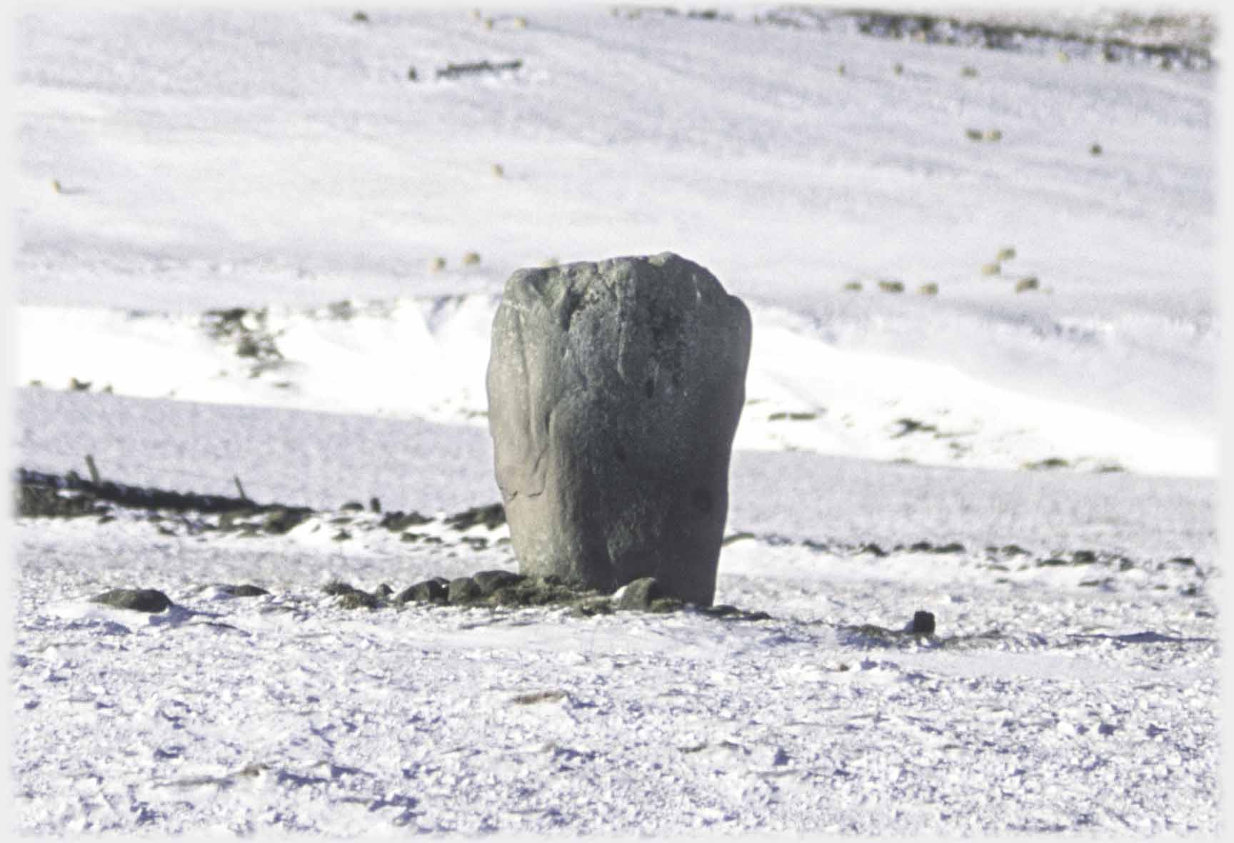 Standing stone in snowy field.