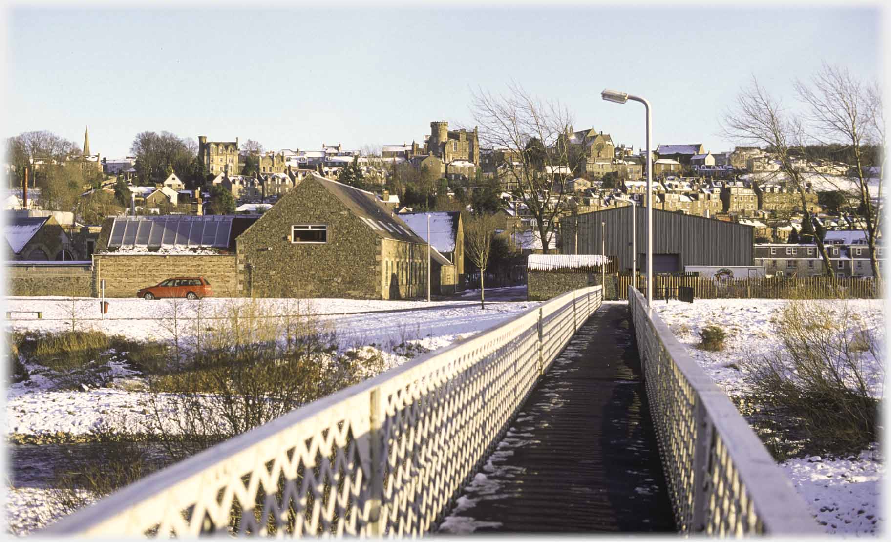 Pedestrian bridge pointing to hillside of building, one turreted on dominates.