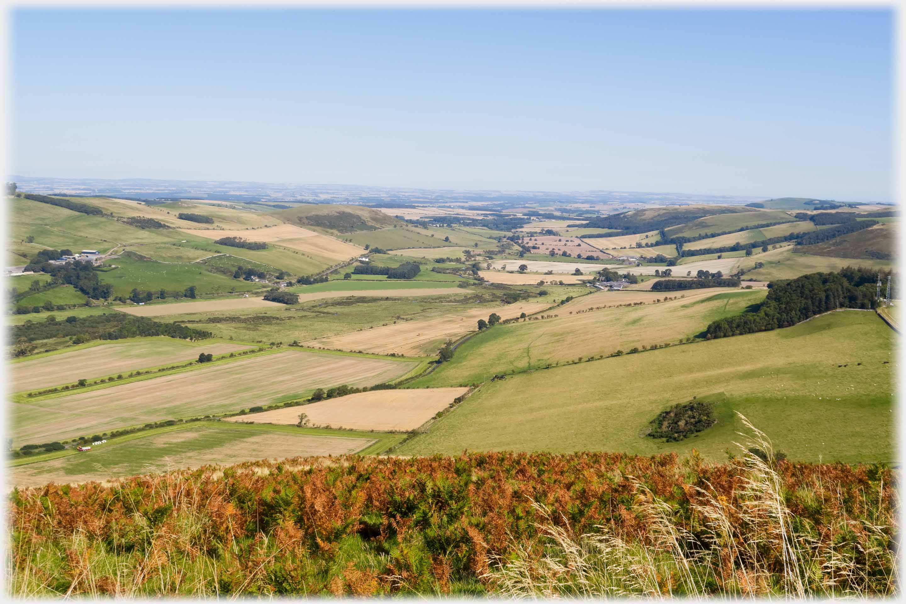 Looking across fields down valley, wide flat expanse of country beyond.