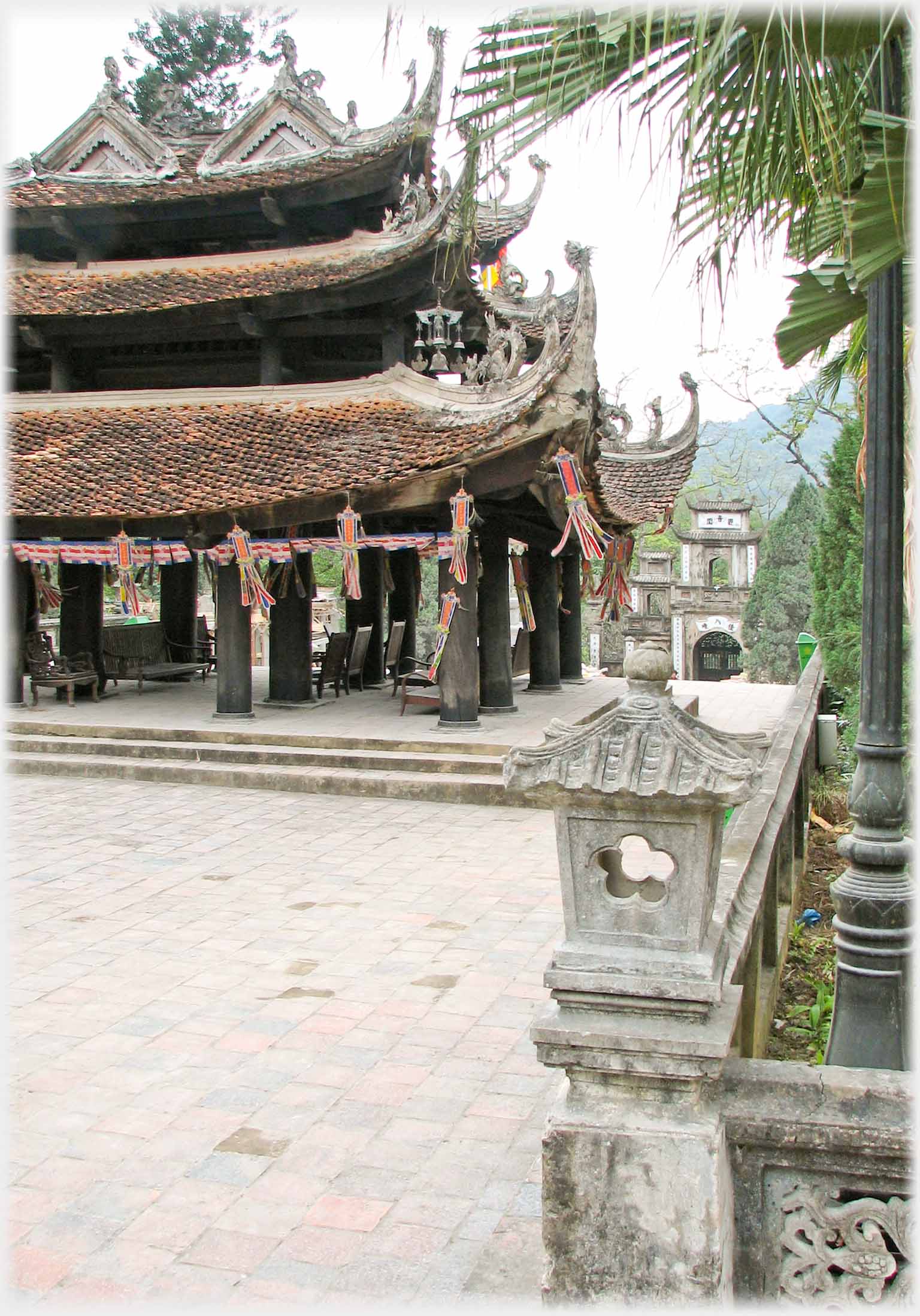 Large three layered roofed building with open pillared ground floor, lantern in foreground, gateway in distance.