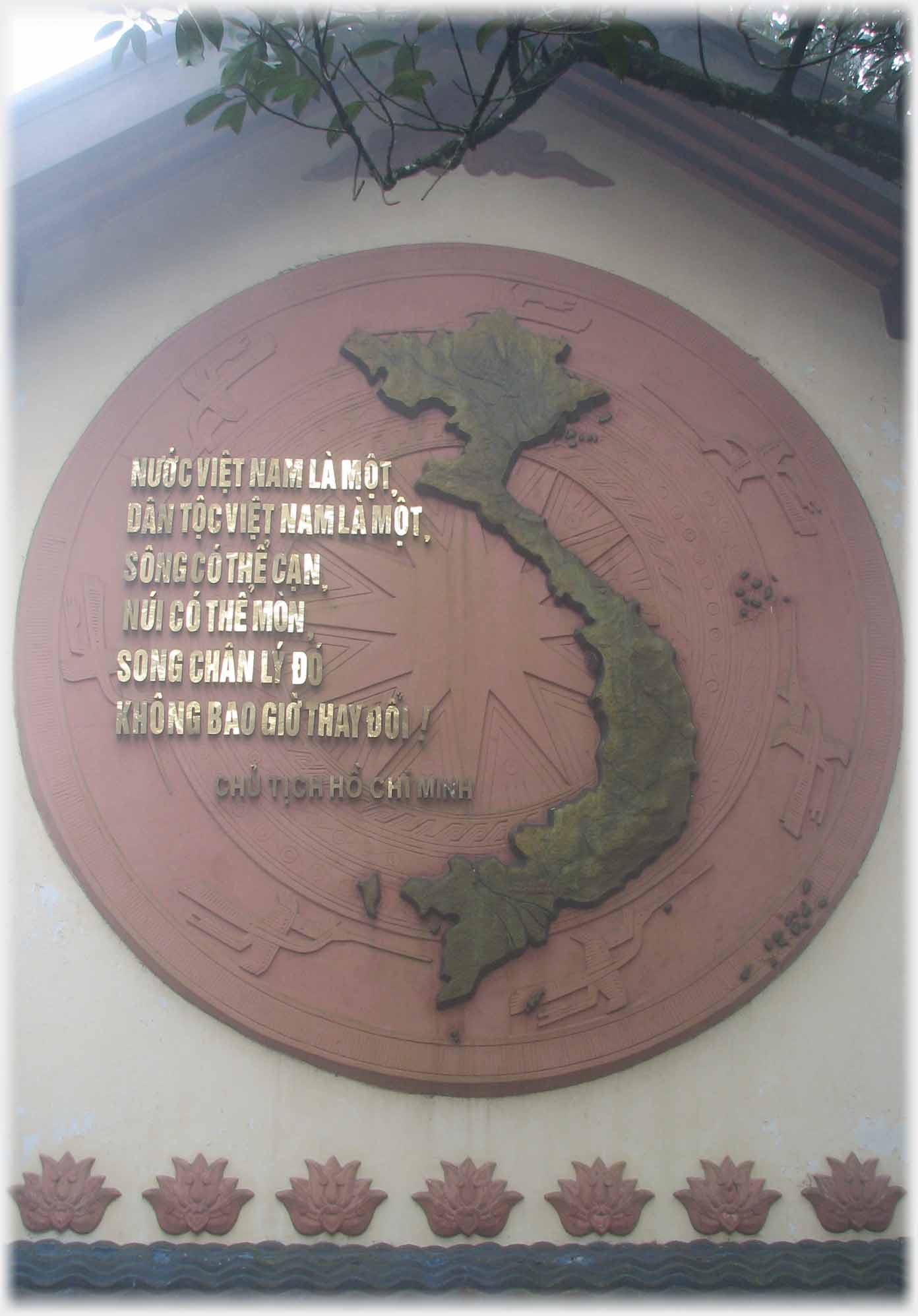 Circular mock drum on end wall of building with raised map of Vietnam and rasied glden writing.