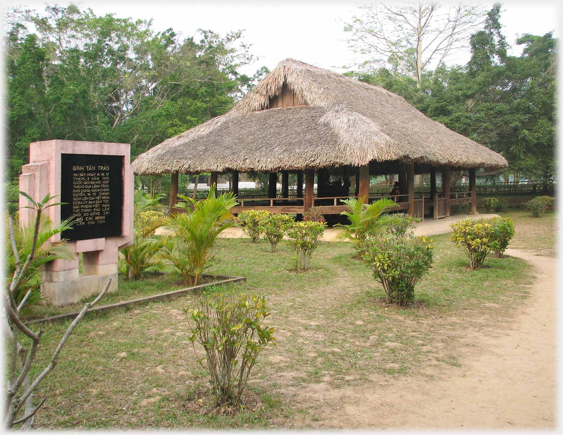 Thatched wall-less building with engraved mounted black stone next to it.