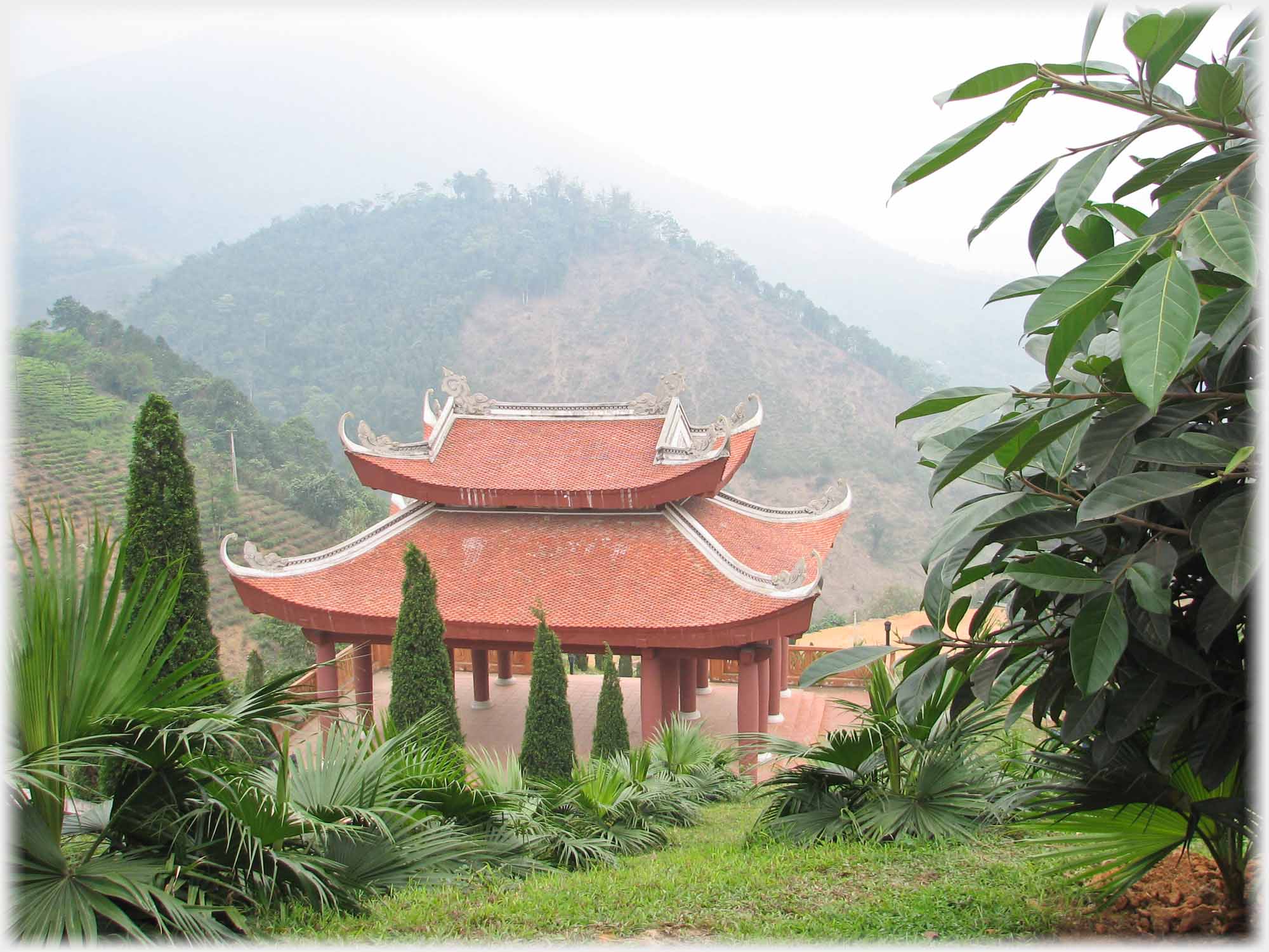 Double roofed open sided building supported by pillars, hills beyond.