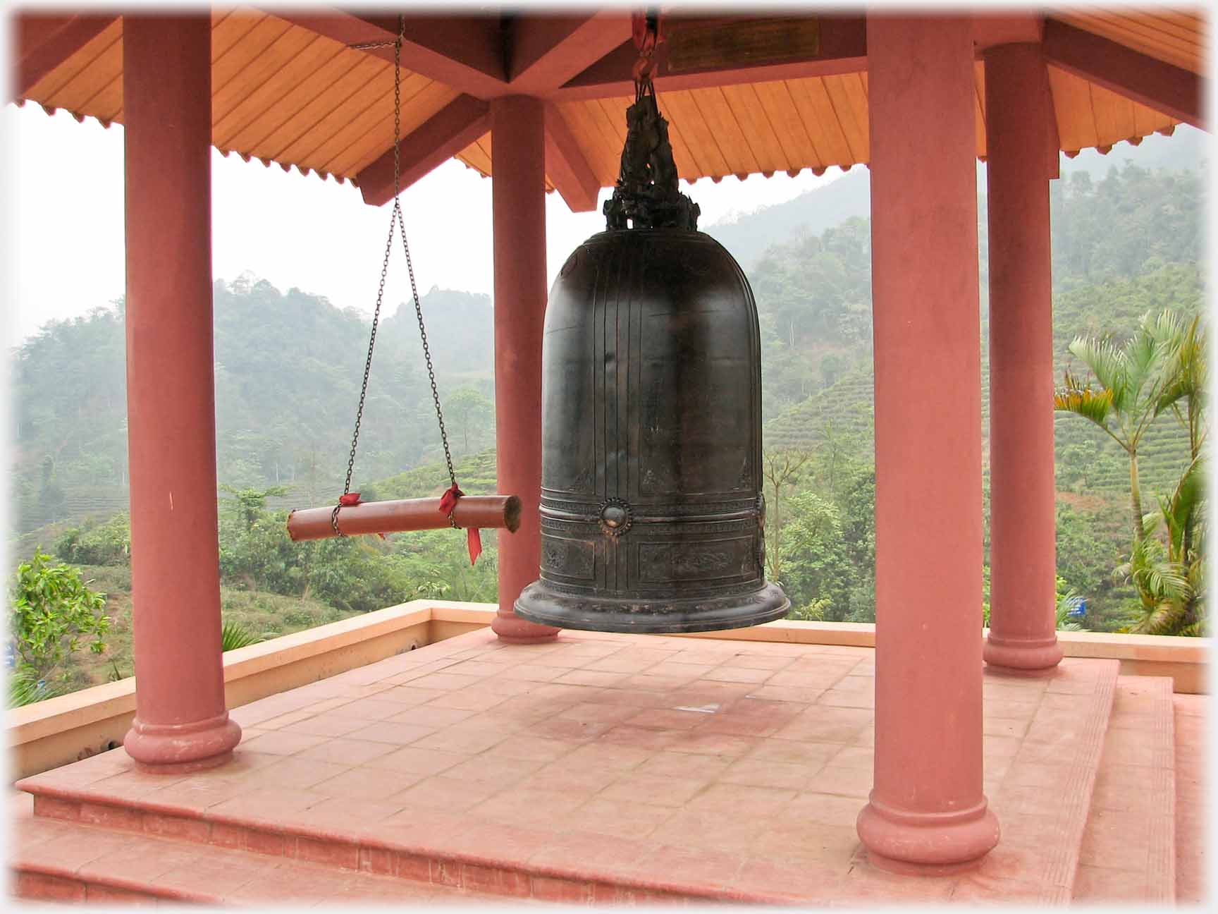 Large bell hanging in open pavillion, with log hanging next to it.