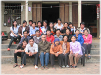 Large group of people sitting in tiered rows in front of house.