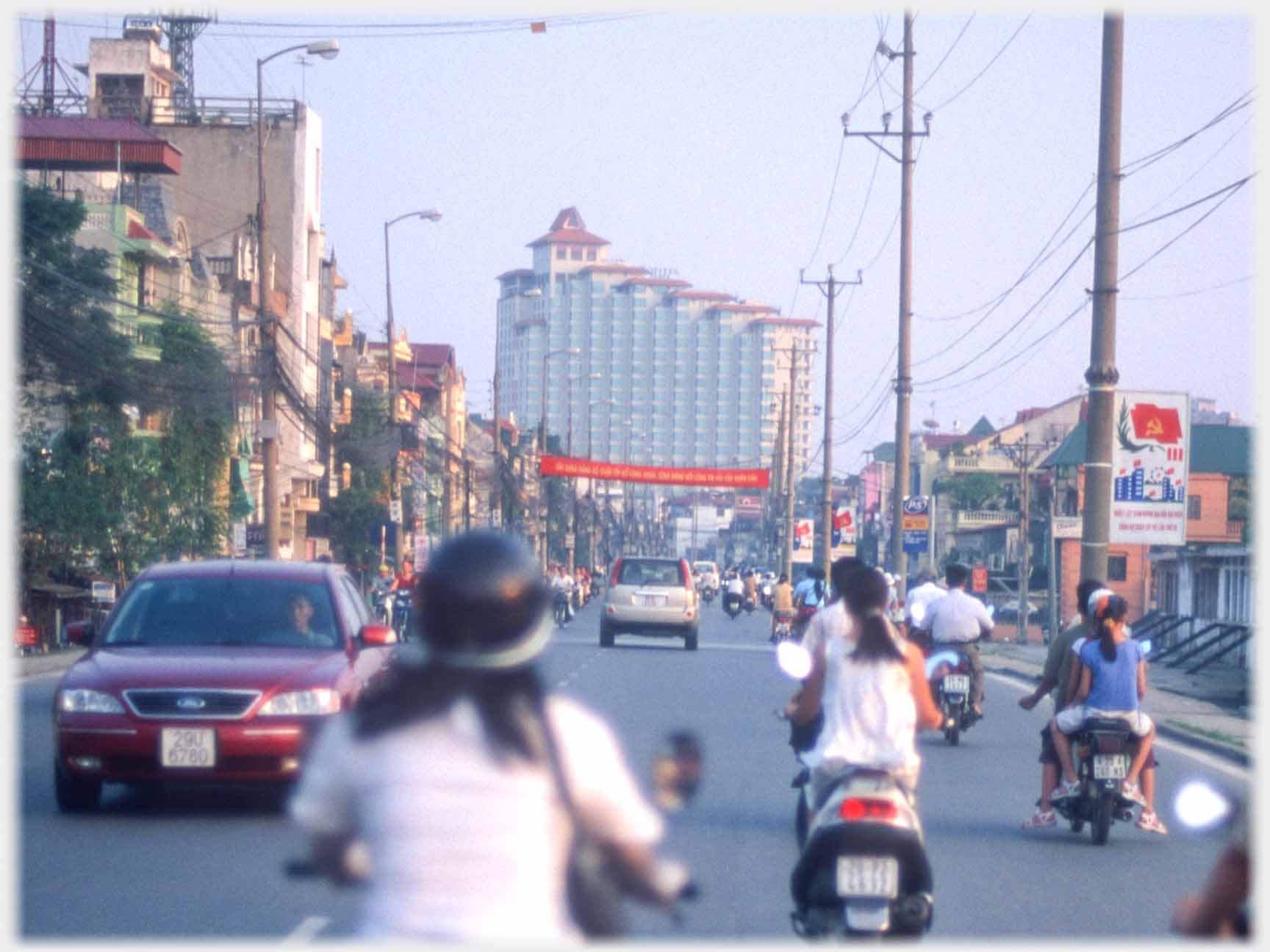 Road busy with motorbikes pointing it very large building.