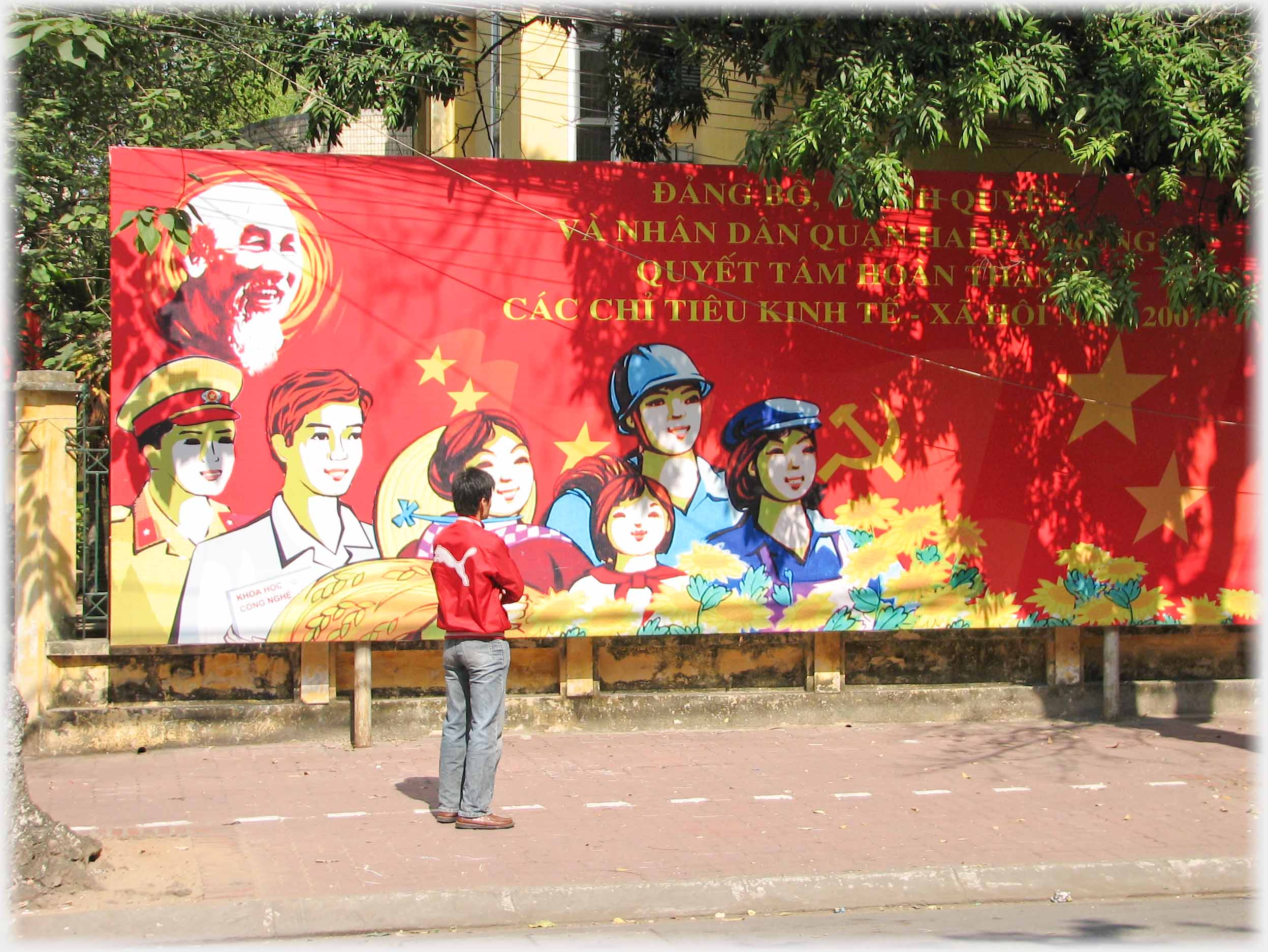 Man standing looking at large red banner with happy styaliseed workers, three metres high by seven metres, Ho Chi Minh in top corner.