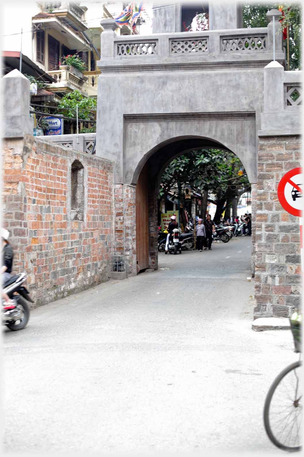 Curved arch, covered in concrete, gateway with brick walls leading to it.