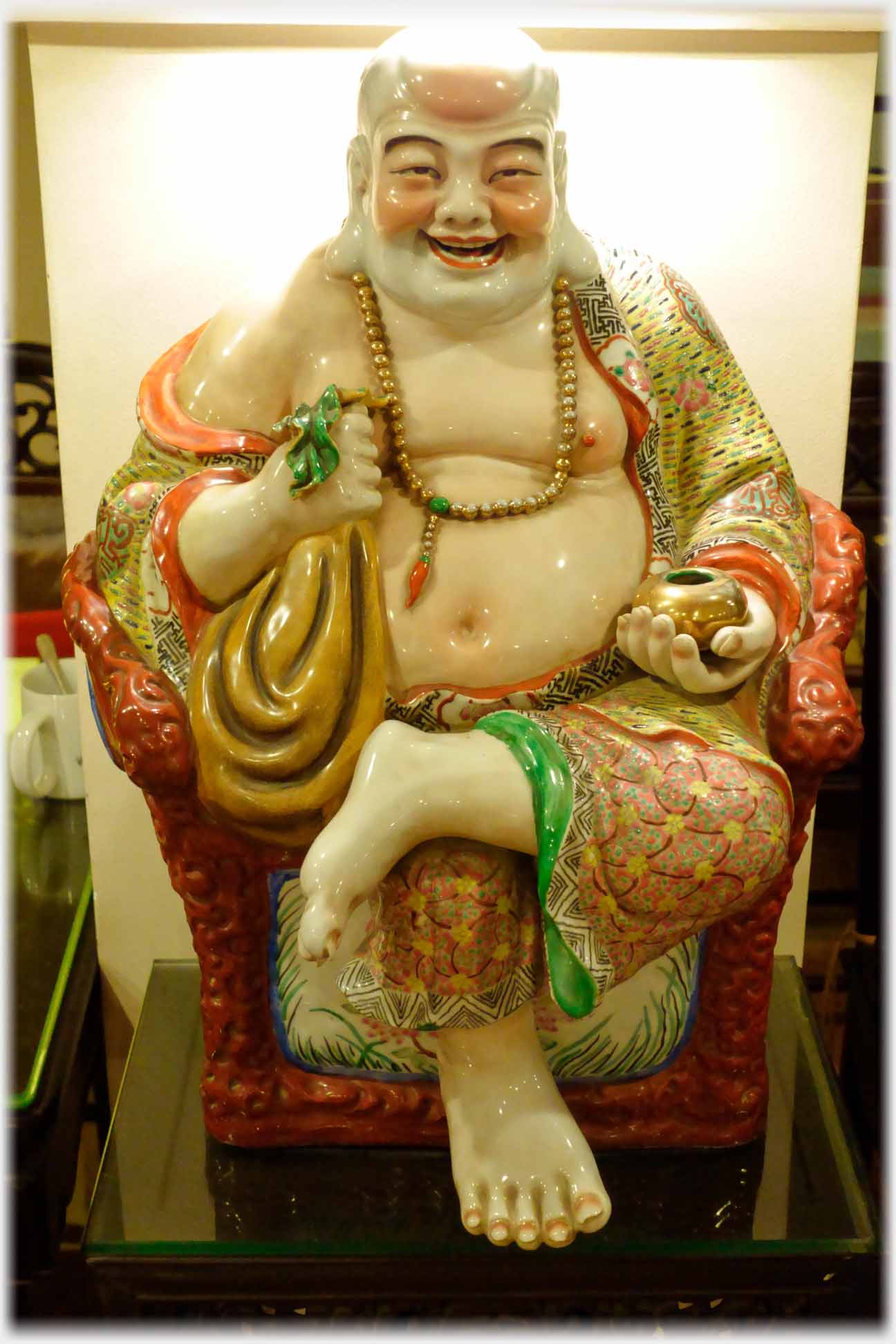 Laughing plump Buddha figure sitting in chair holding bowl and ribbon.