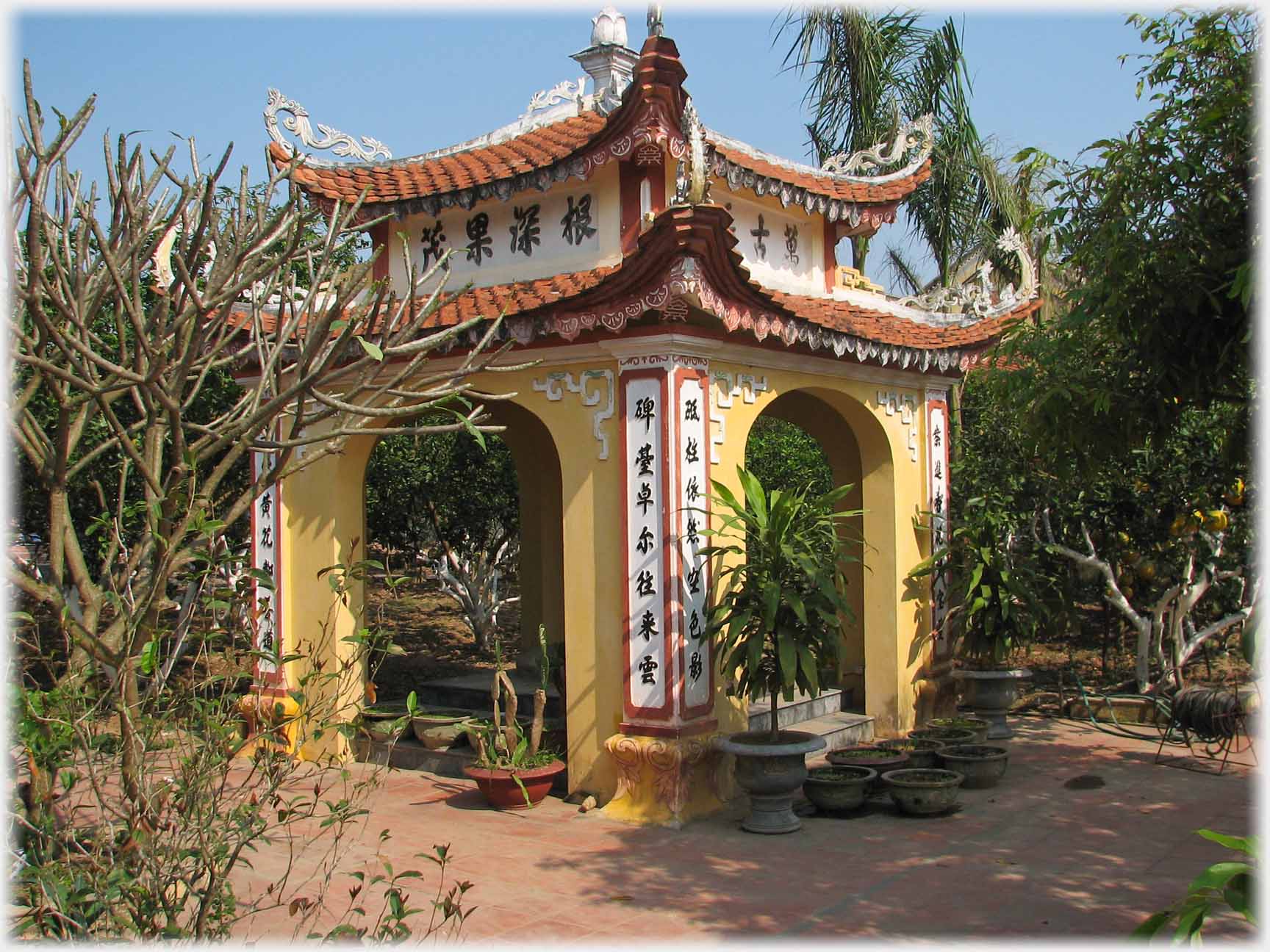 Square roofed building in garden with four full arches and elaborate roof.