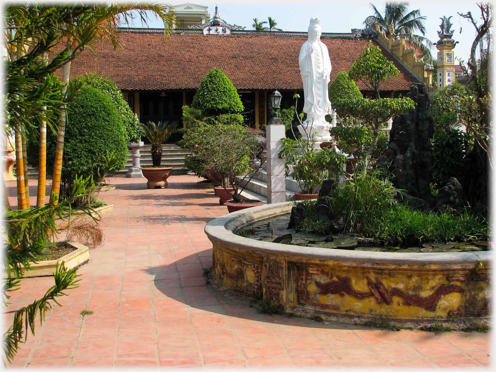 Garden wtih pond on right and standing white Buddha in front of building.