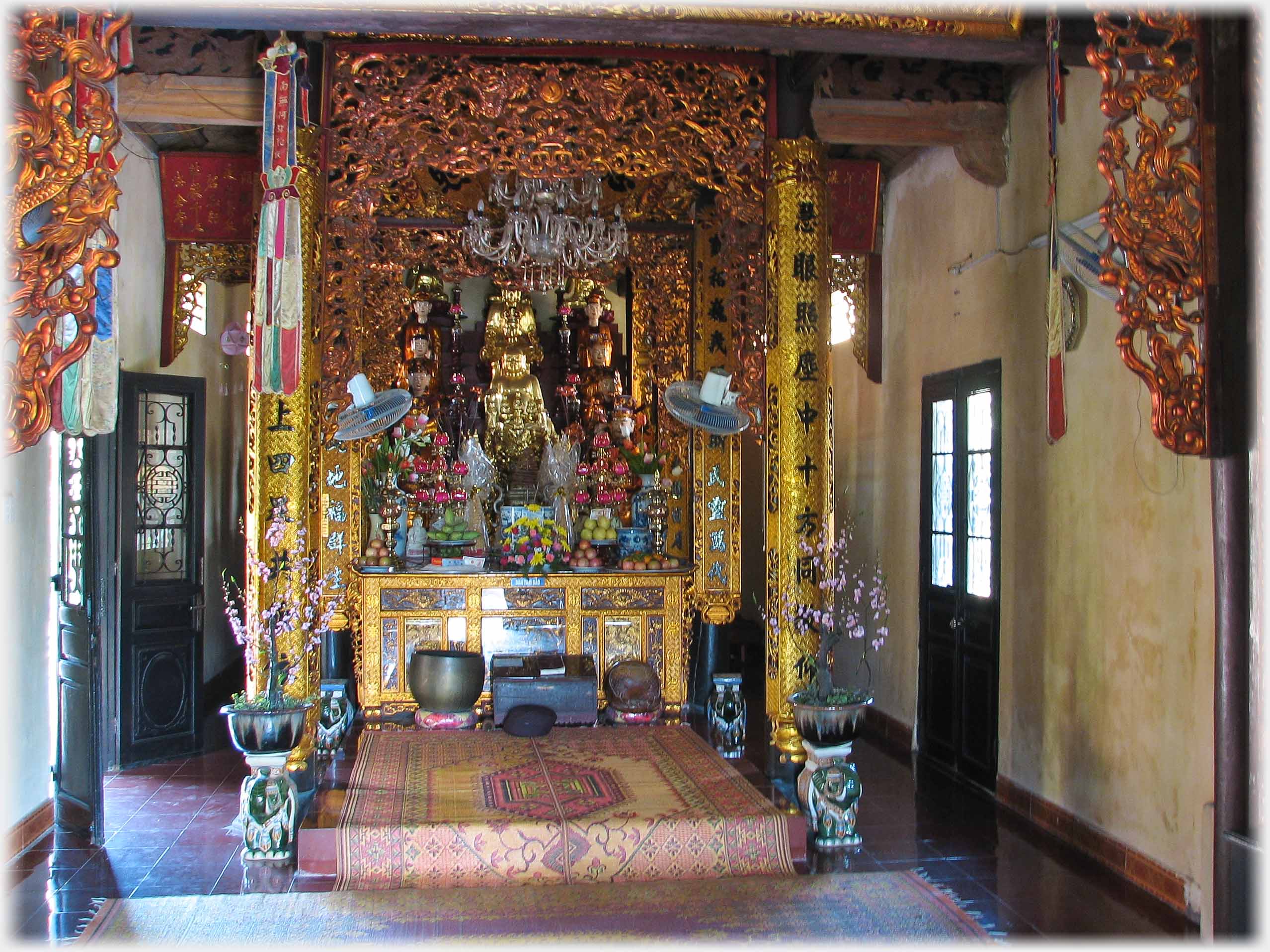 Highly gilded altar with dishes of fruit, gilded decorative beams, doors and display pots with plants.