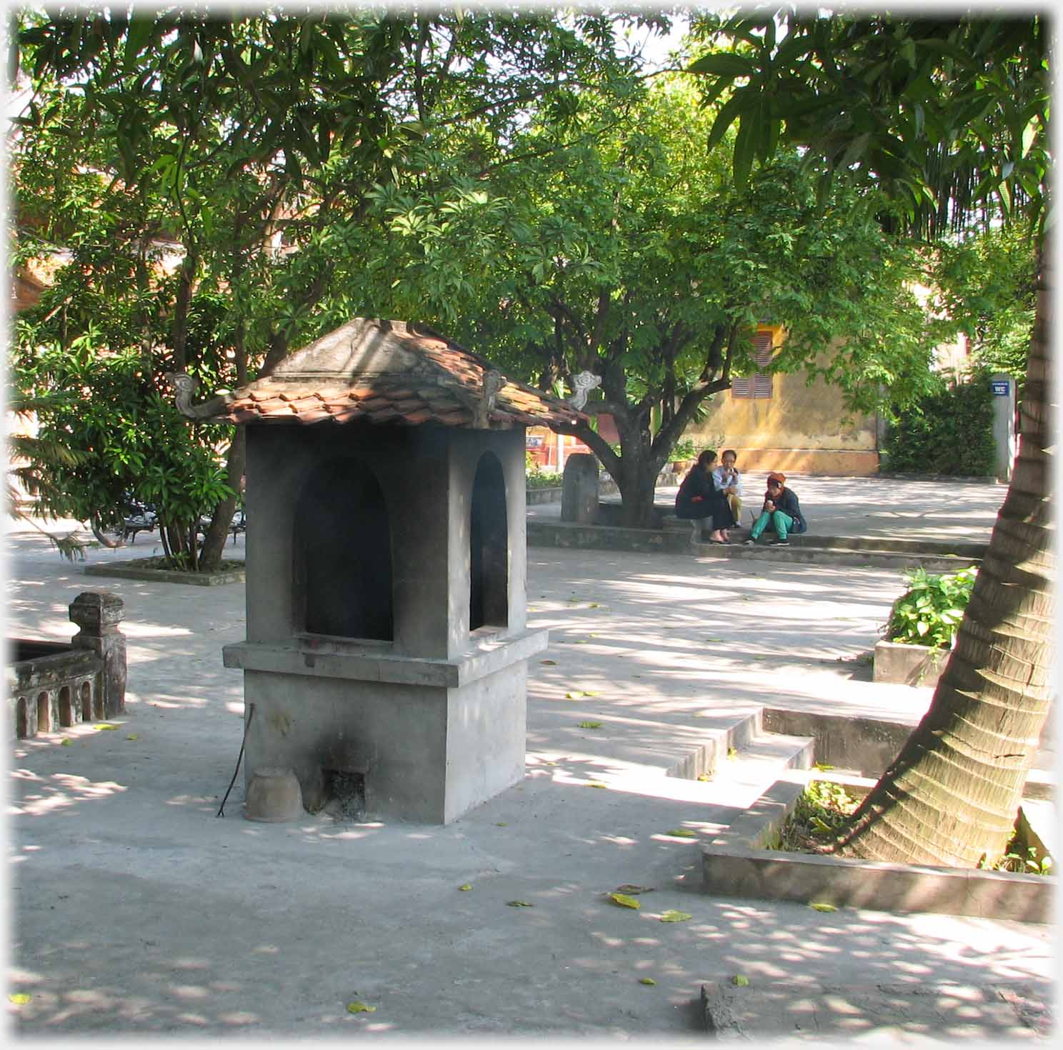 Square high roofed fireplace in centre of courtyard, small group beyond.