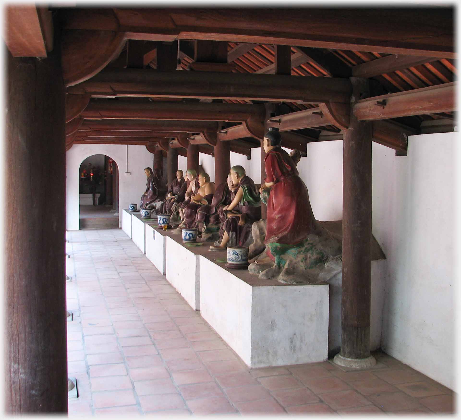 Five sets of statues on plinths in beamed gallery by colonnade.