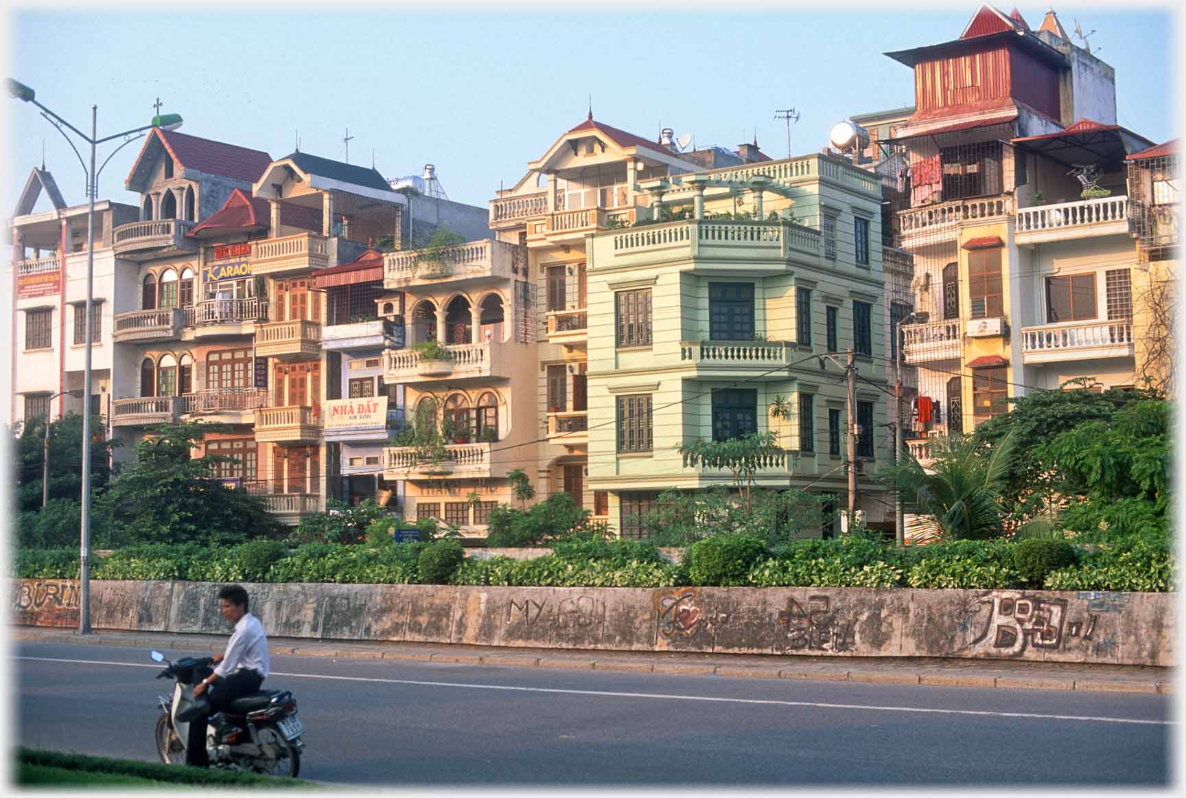 Row of four and five story town houses with wall along road in front of them.