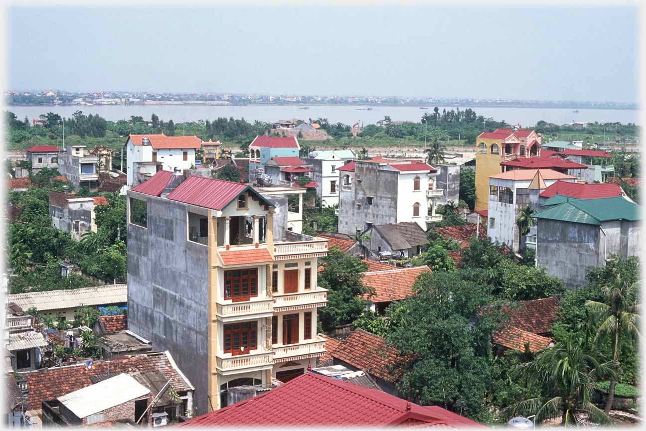 Two four story houses with balconies in foreground, other houses and trees, river in distance.