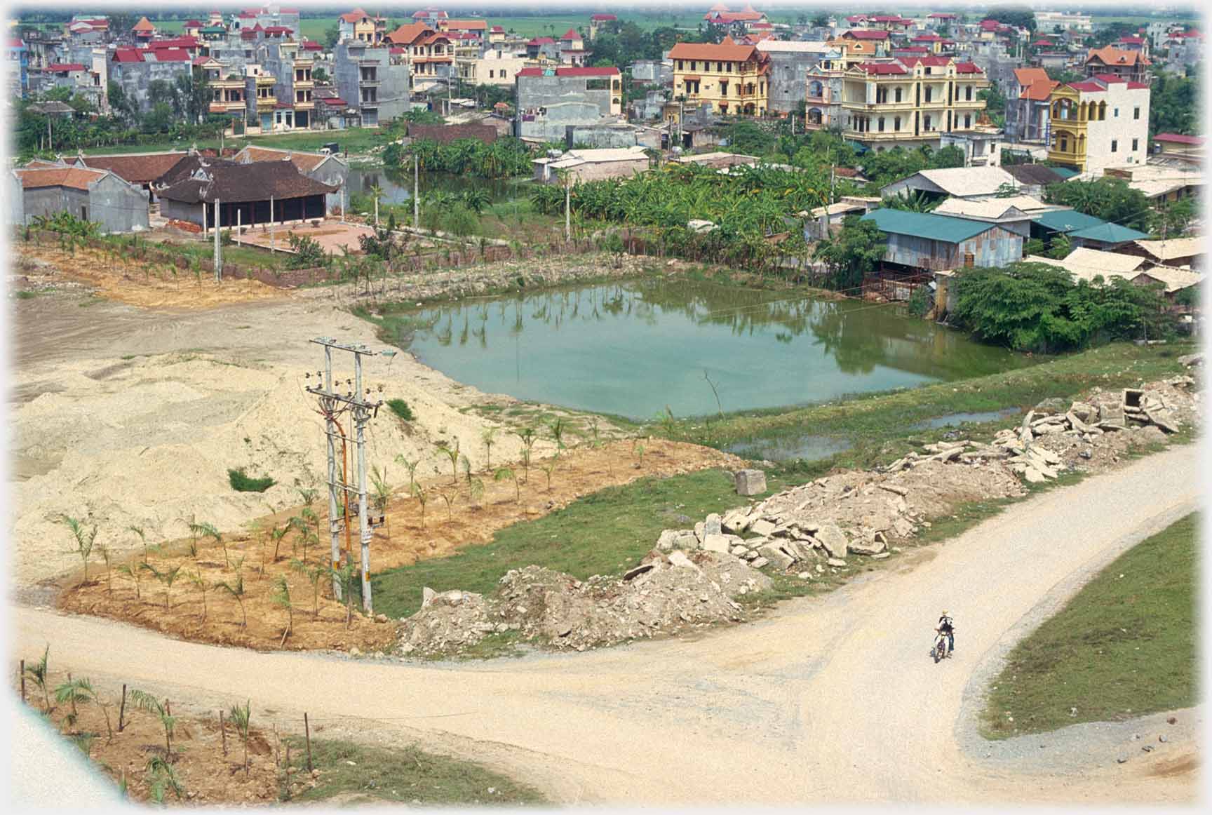 Pool with dusty roads and cleared area nearer, houses beyond.