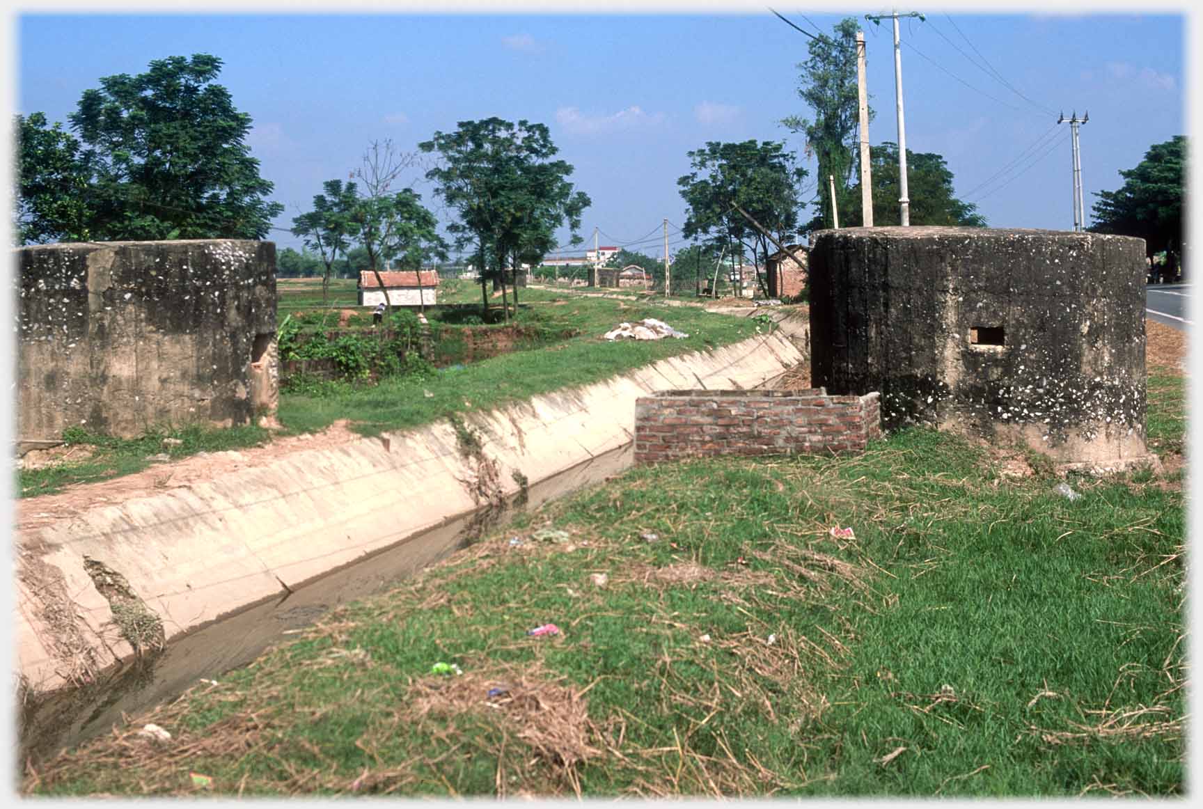 Channel with concrete banks and two black concrete hexagonal buildings with tiny window.