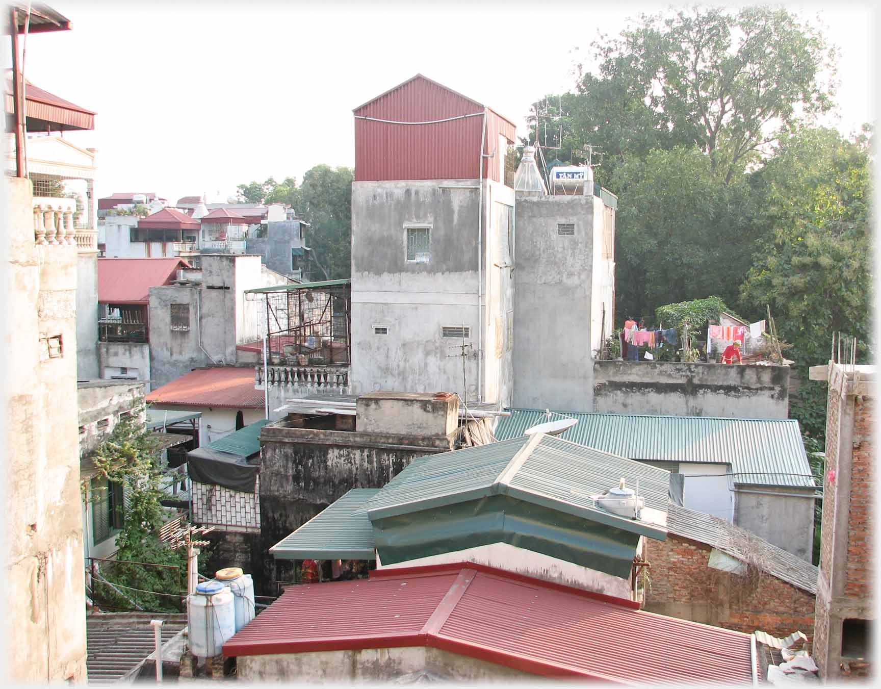 Roofs, house rising above, washing on roof, trees.