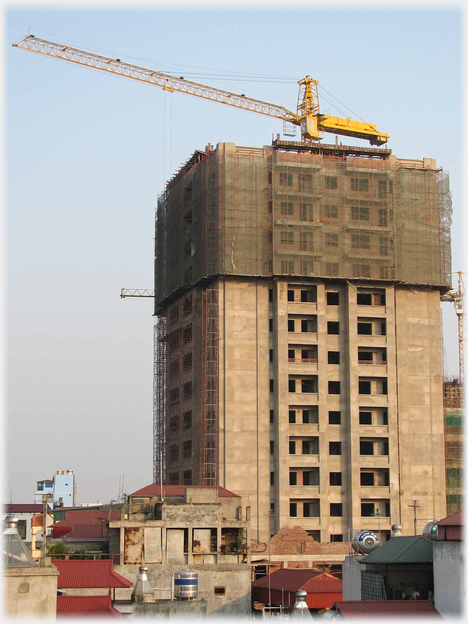 Single tower block of about 15 stories with crane over it and netting around top four stories.